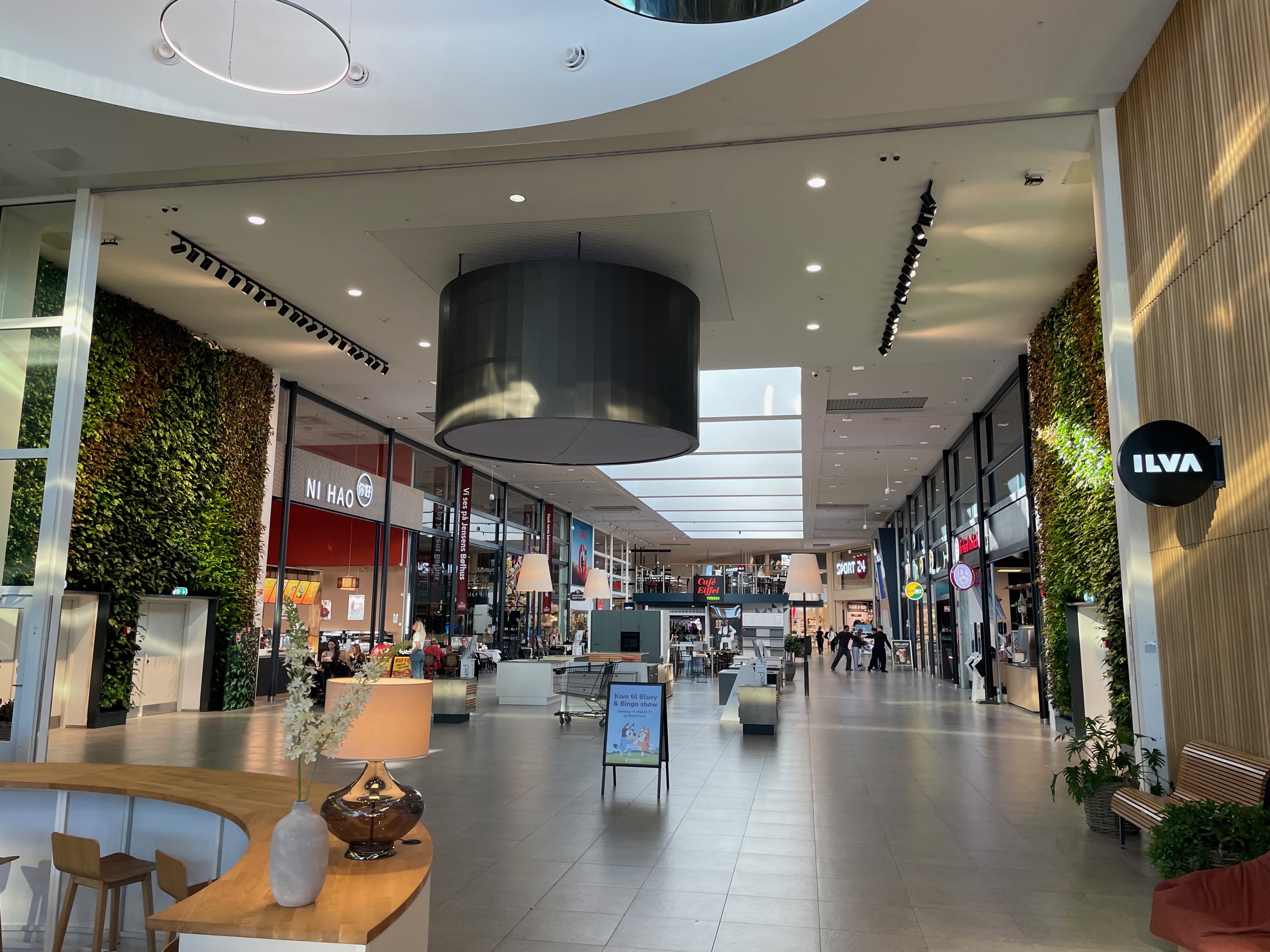 Jensens Bøfhus Kolding review view inside Kolding Storcenter, showing the shopping mall walkway with ILVA, NI HAO, Sport 24, Café Eiffel, green wall decor, seating areas, and nearby restaurant spaces