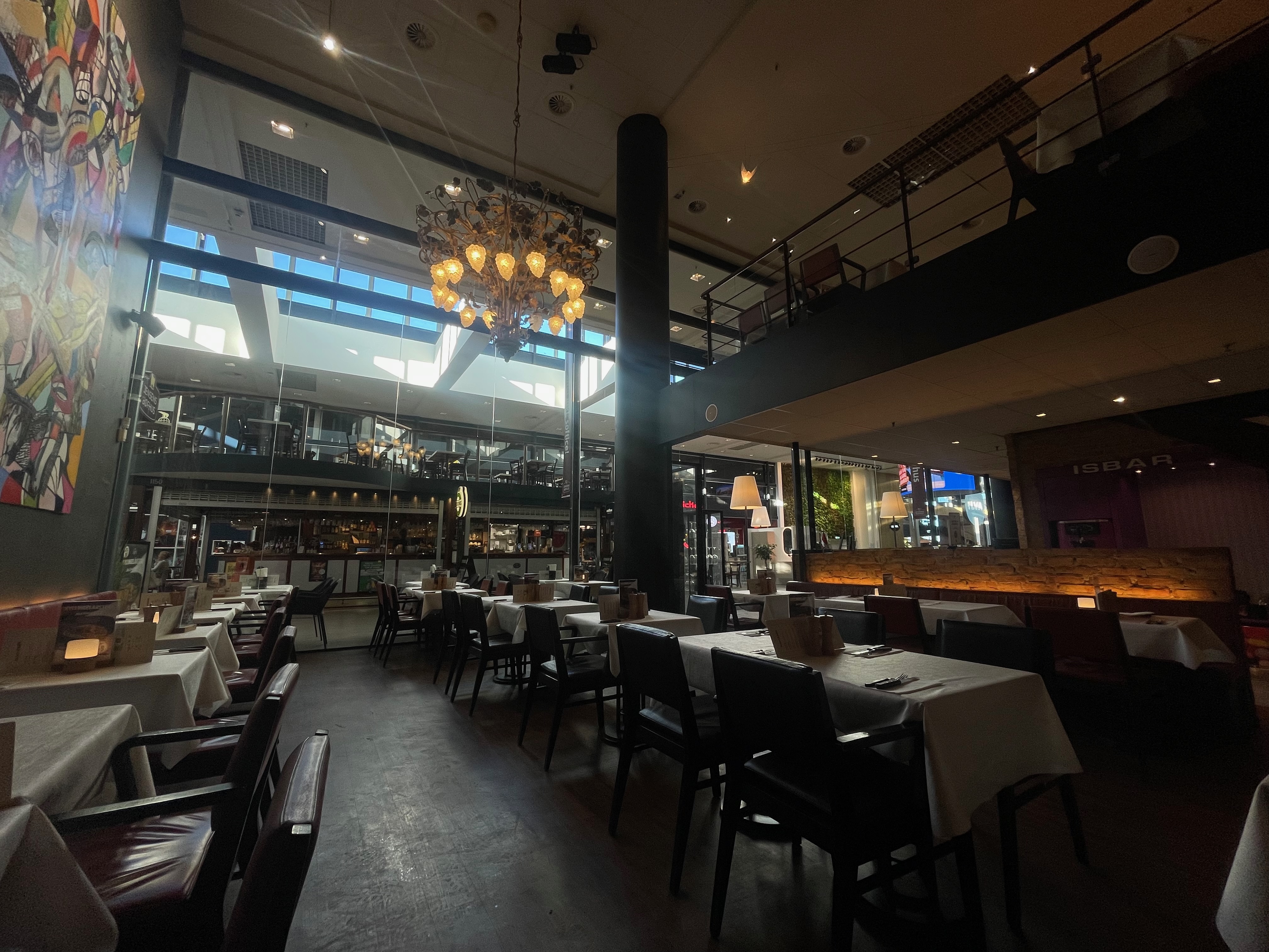 Jensens Bøfhus Kolding review wide interior view inside Kolding Storcenter, showing the former steakhouse dining area with white tablecloths, red booth seating, black chairs, chandelier lighting, and shopping center windows