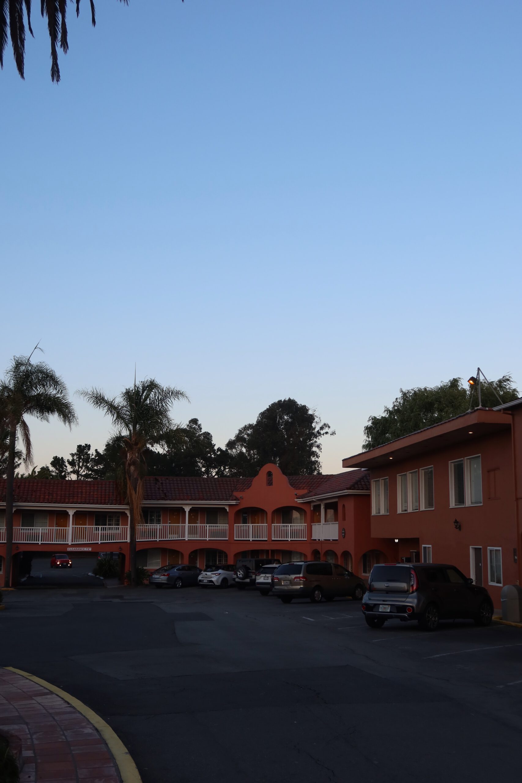 Exterior courtyard of SFO El Rancho Inn near San Francisco Airport with parked cars and palm trees at dusk
