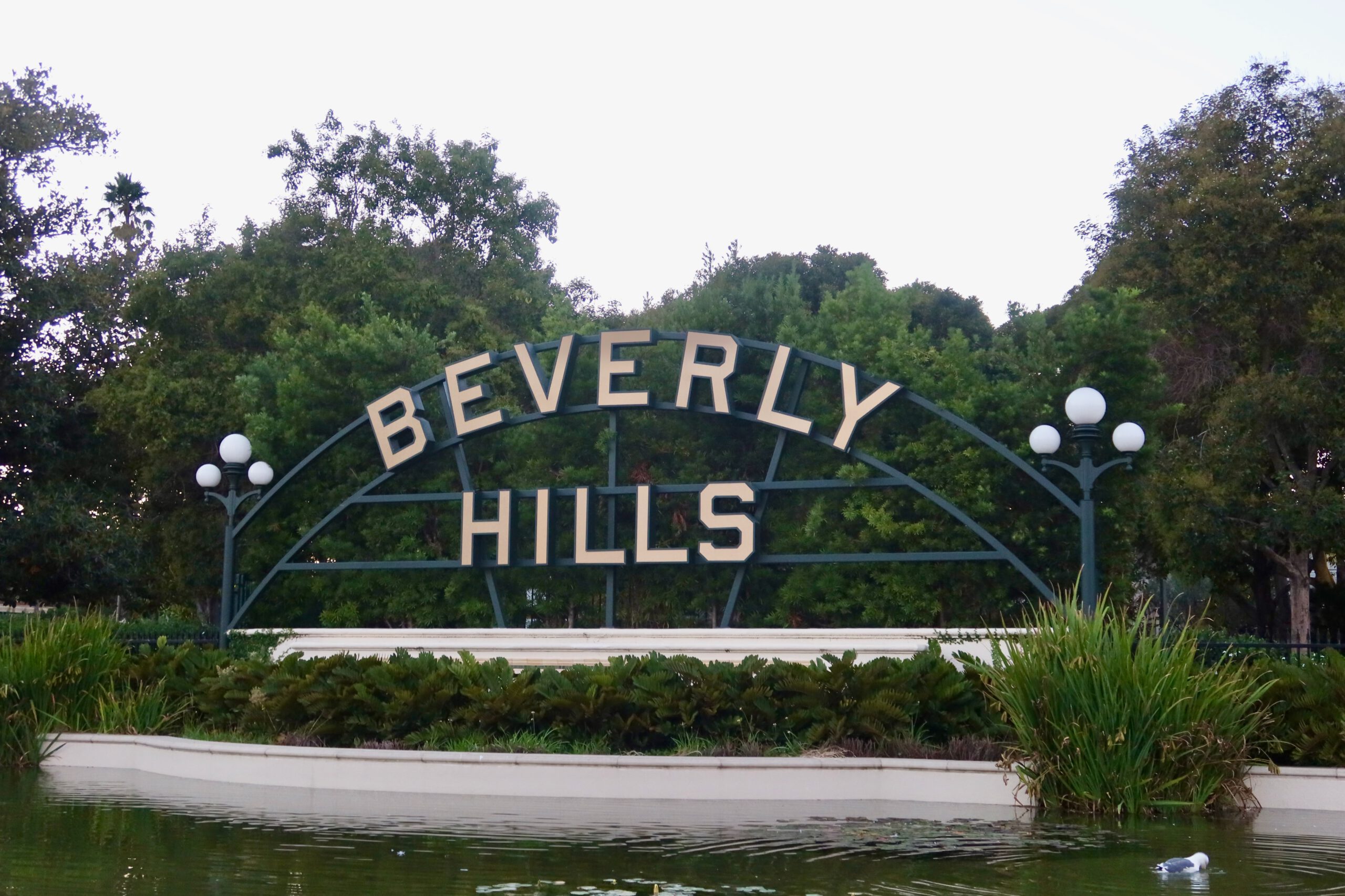 Beverly Hills sign at Beverly Gardens Park with trees and pond in the foreground.