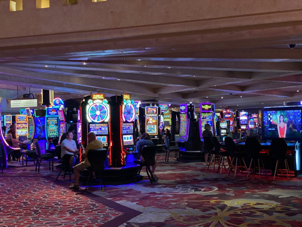 Interior view of the MGM Grand Las Vegas Casino featuring rows of colorful slot machines, illuminated gaming displays, and visitors playing under the iconic low-ceiling casino floor.
