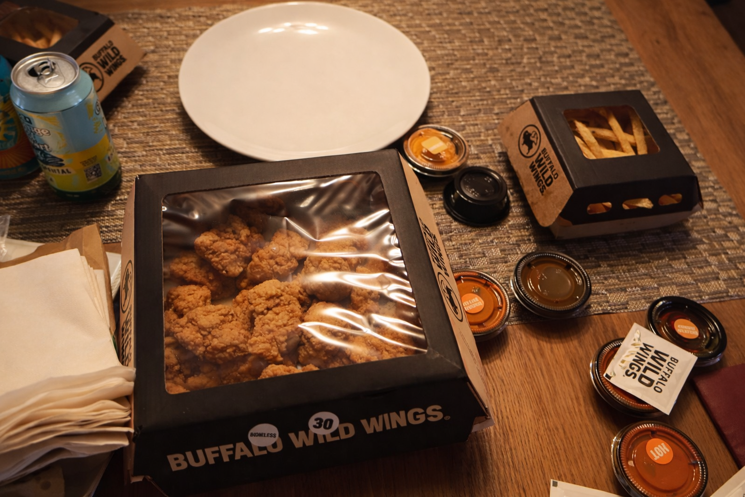 Buffalo Wild Wings Boise Uber Eats order with 30 boneless wings, multiple sauces, fries and drinks on a dining table