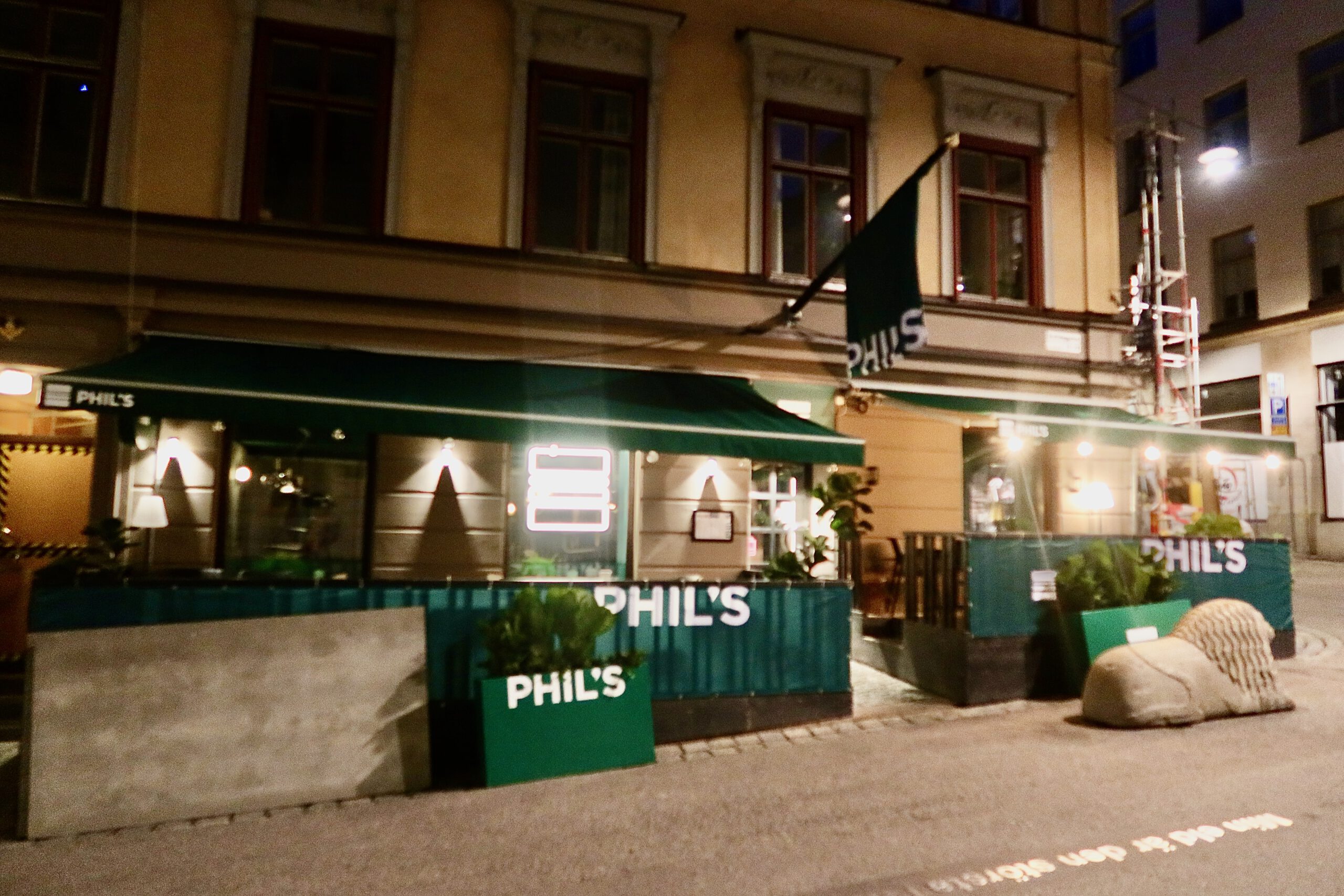 Phils Burger Drottninggatan Stockholm exterior at night, showing the green awnings, terrace seating, and illuminated signage on Stockholm’s main shopping street