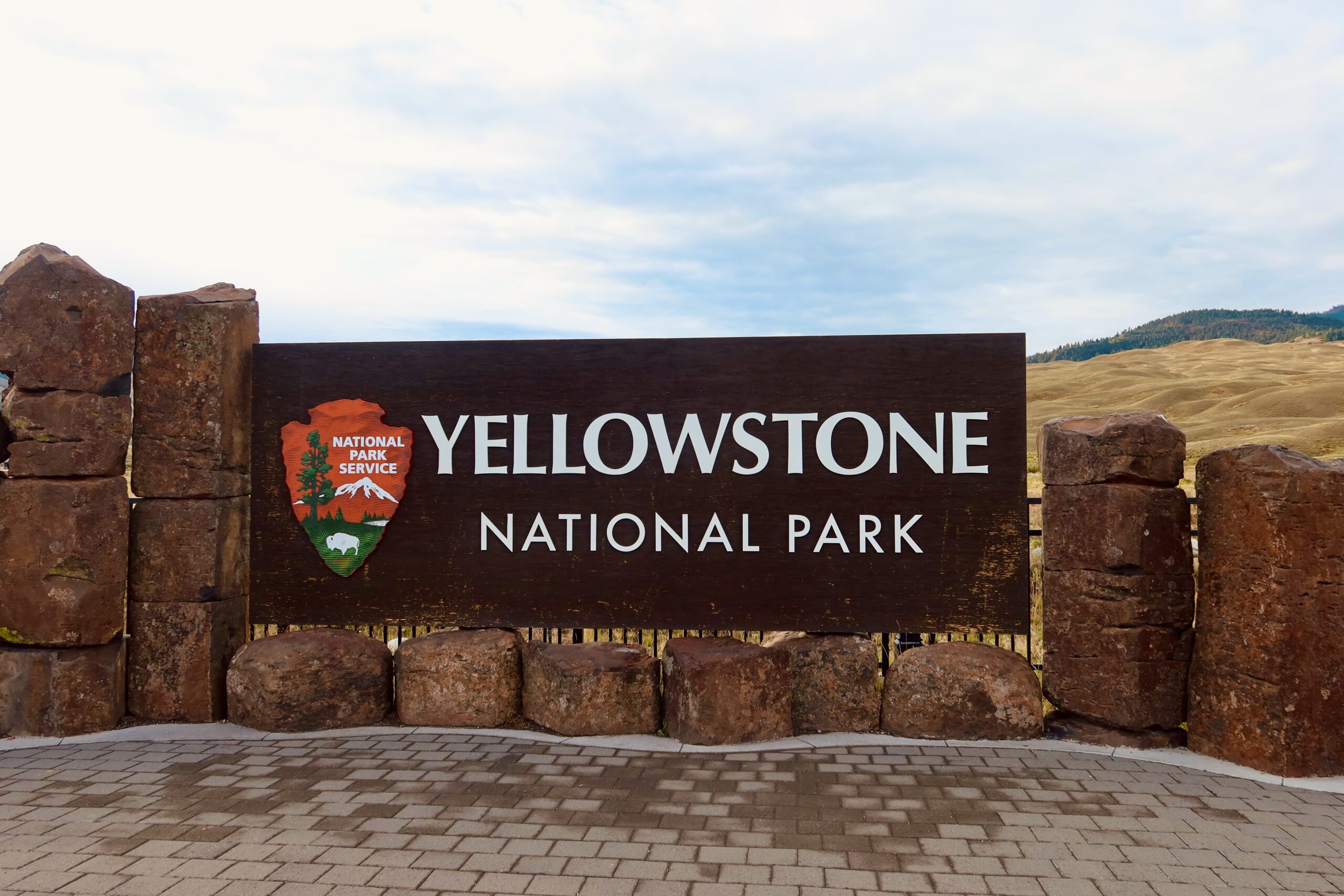Entrance sign of Yellowstone National Park with National Park Service logo, marking the gateway to America’s first national park, surrounded by open landscapes and iconic western scenery
