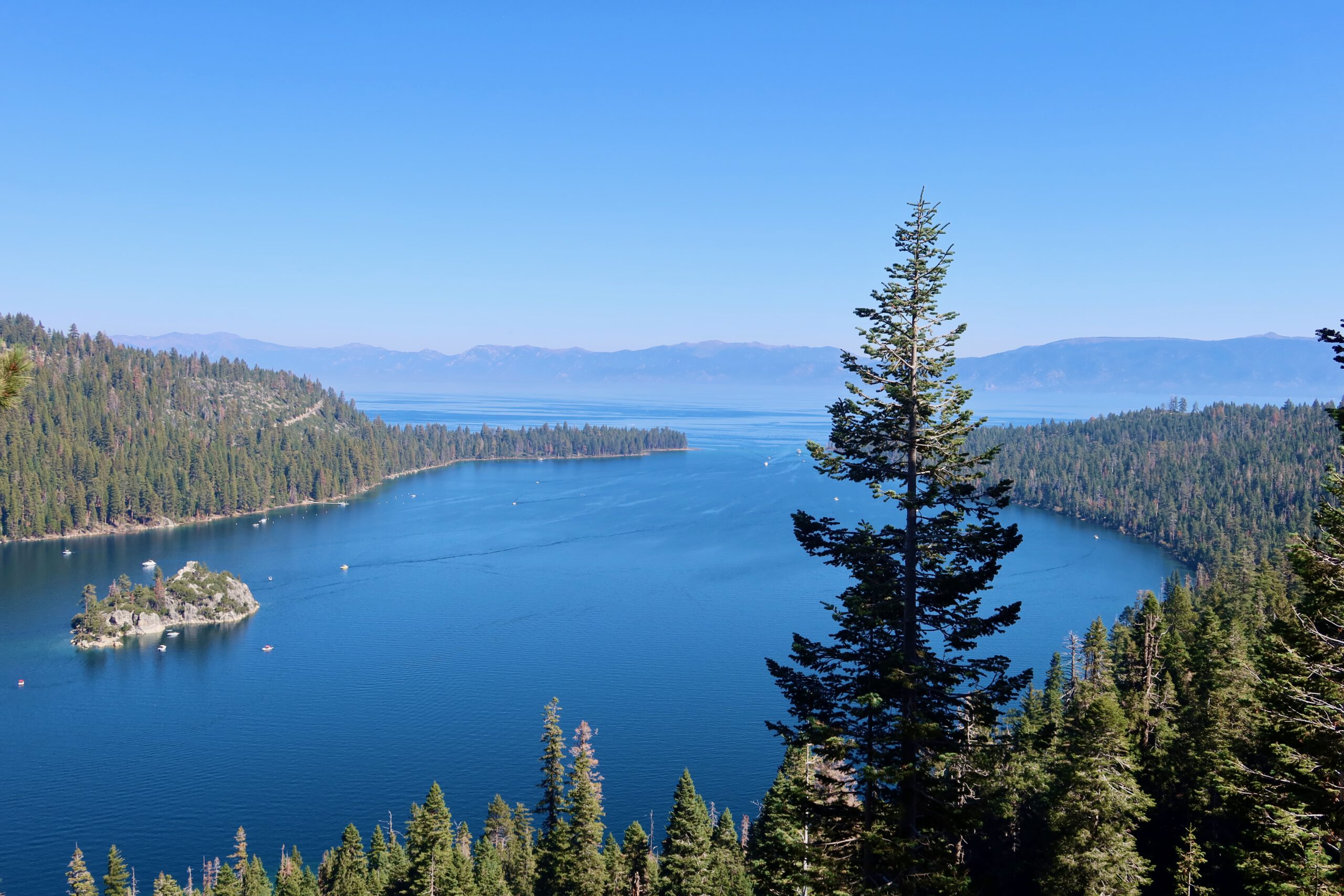 Panoramic view over Lake Tahoe with deep blue water, forested mountain slopes, and the Sierra Nevada skyline on a clear day in California.