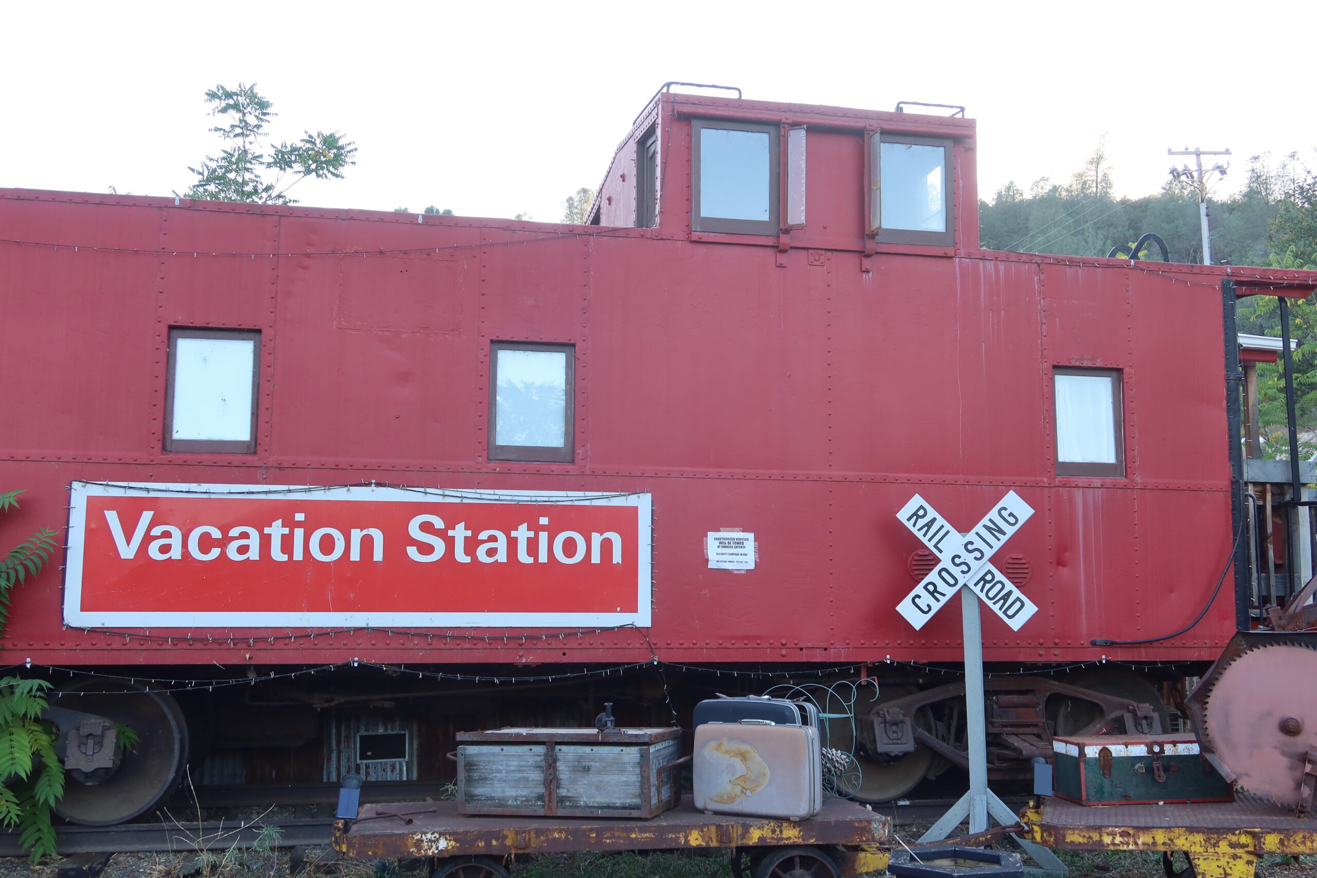 Vacation Station Coulterville caboose exterior, historic red train car with Vacation Station sign and railroad crossing, unique Airbnb stay near Yosemite National Park in California