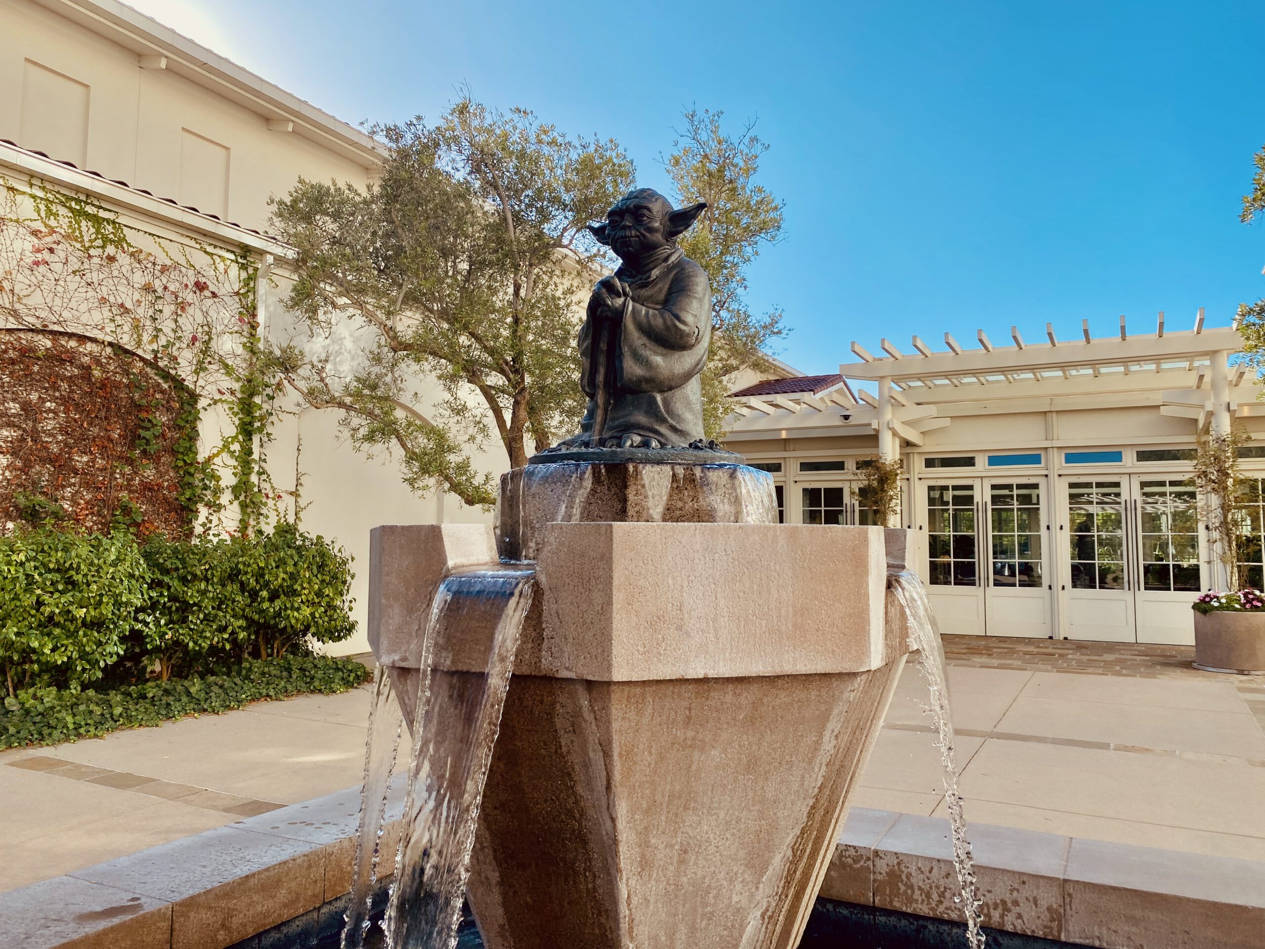 Yoda Fountain San Francisco courtyard view, bronze Yoda statue surrounded by modern architecture, trees and calm Presidio atmosphere