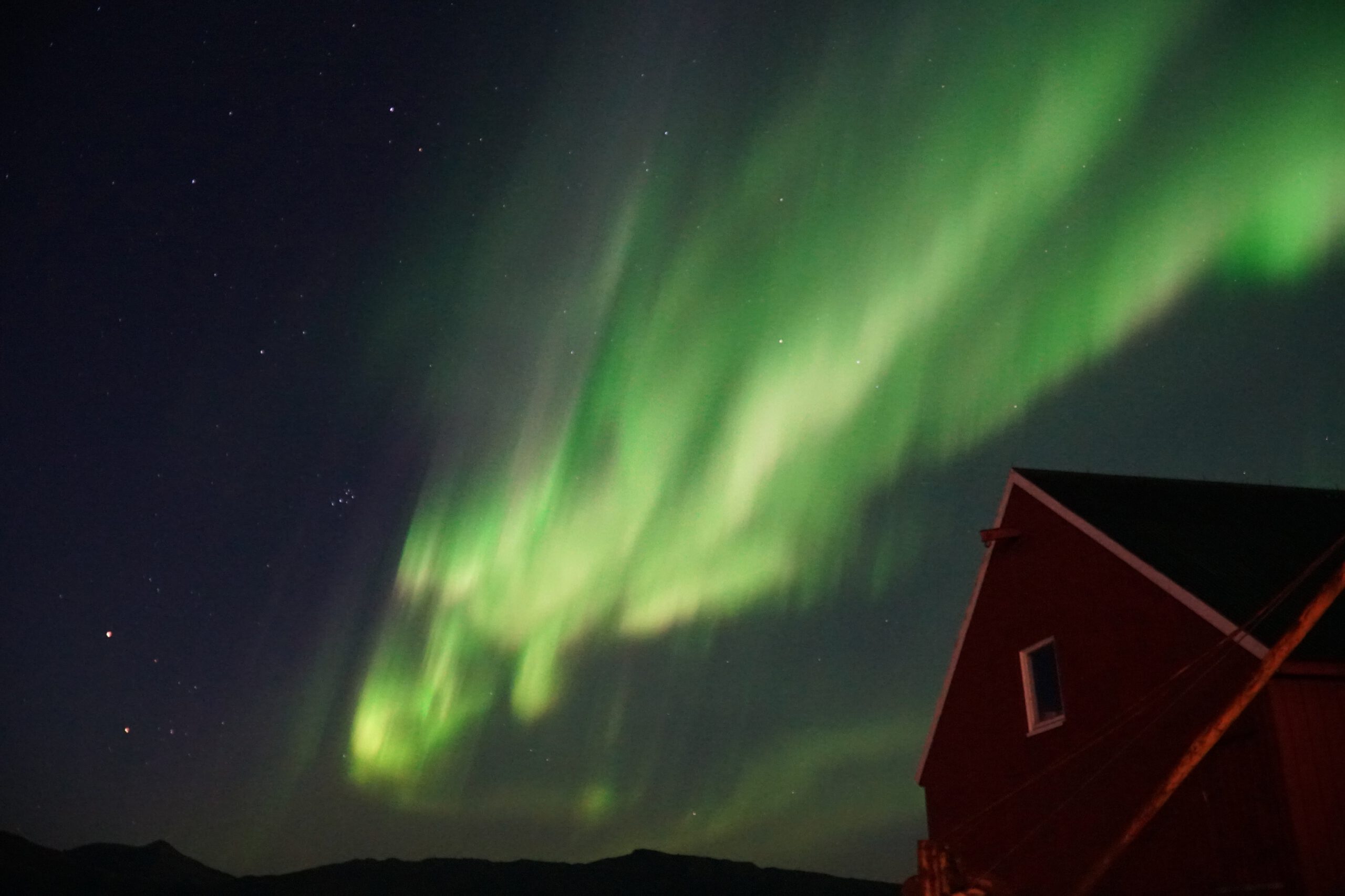 Northern Lights above Lødingen Brygge Hotel Norway, green aurora in the night sky with a wooden building in the foreground in Northern Norway