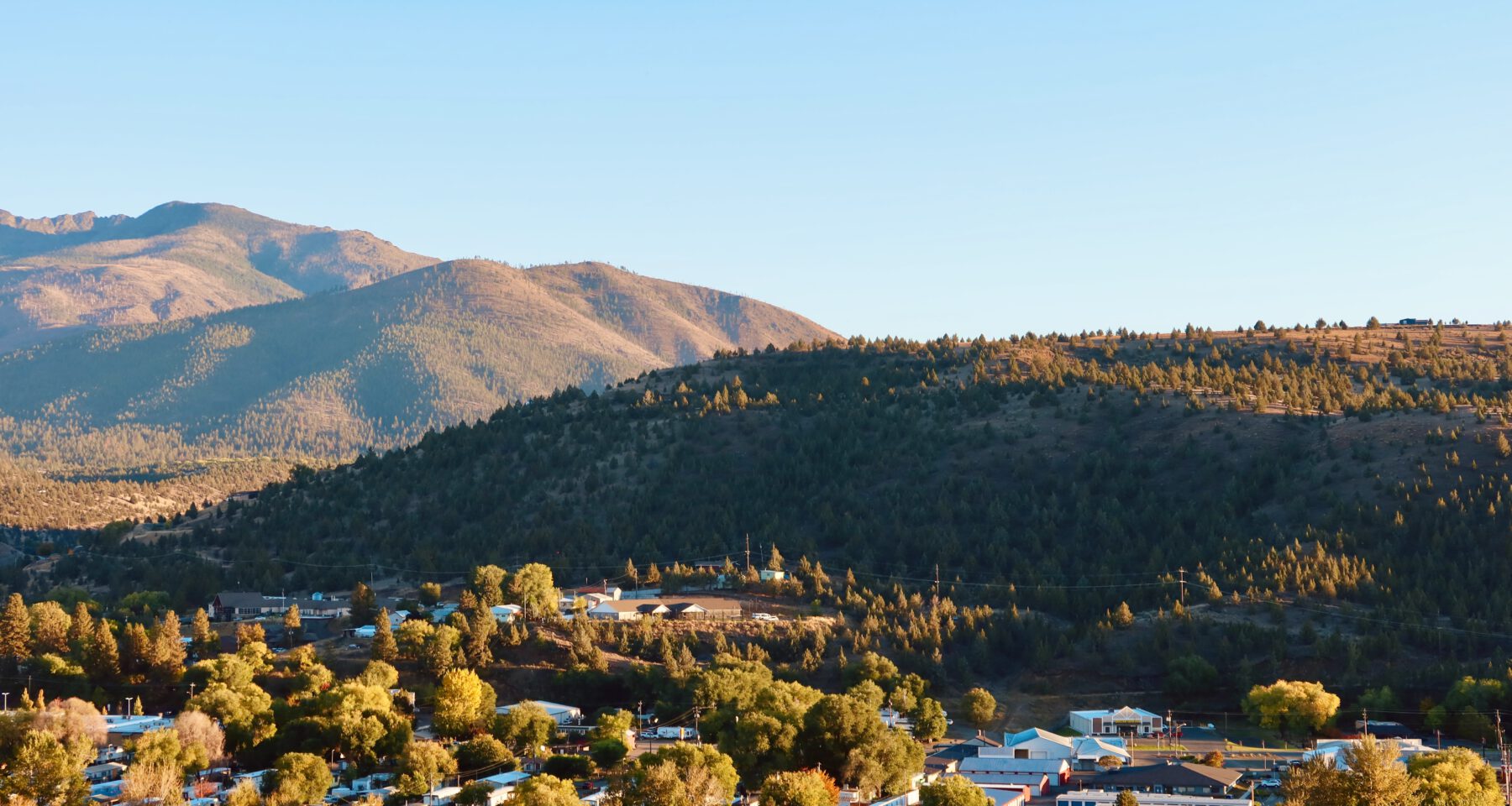 John Day Oregon guide header image showing the small town of John Day surrounded by sunlit hills and mountain scenery in Eastern Oregon