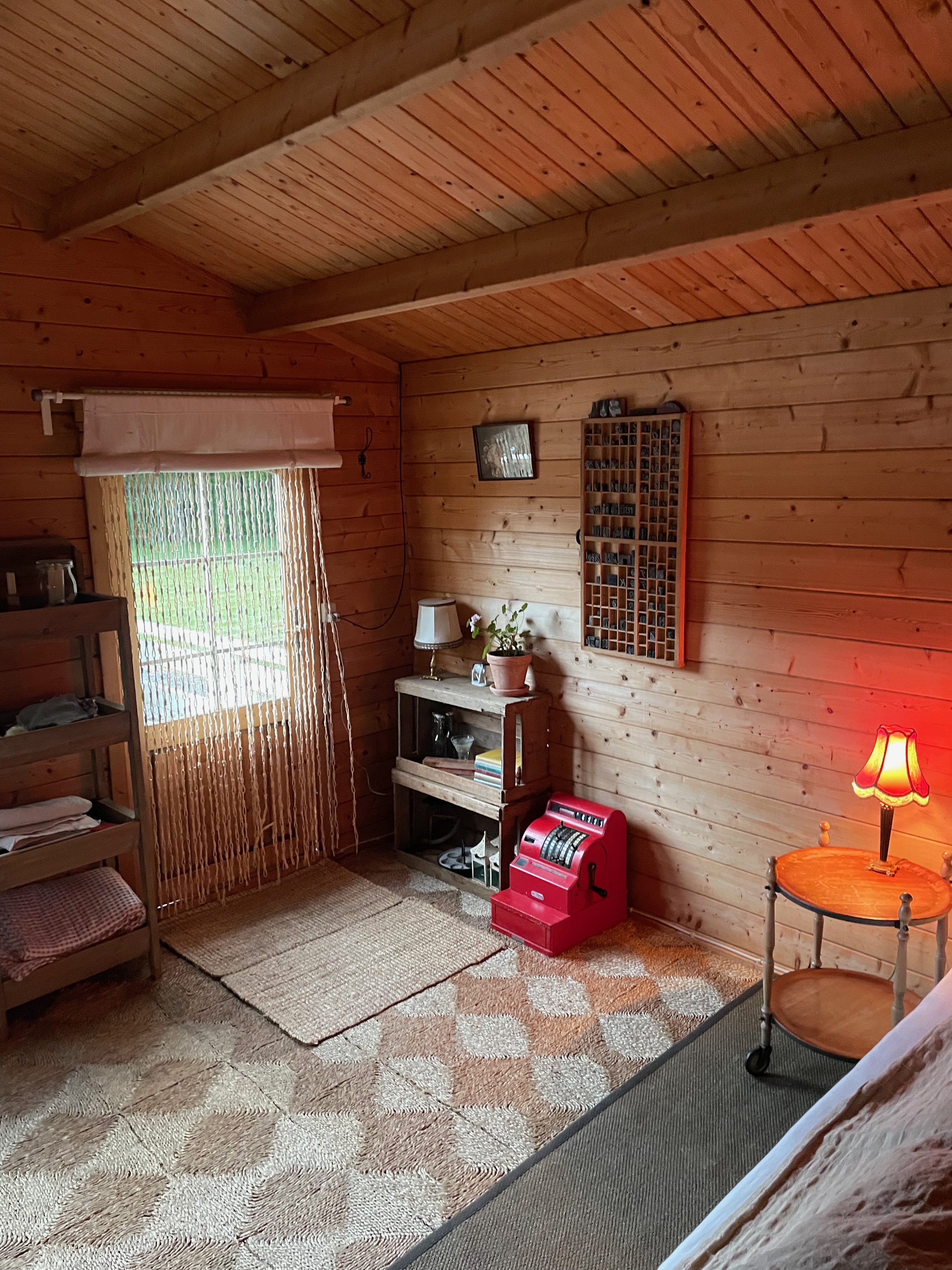Annekset pa Langholm review showing rustic wooden Airbnb hut details with wood walls warm lamp bed corner shelving old red cash register and cozy interior in Ringe Denmark