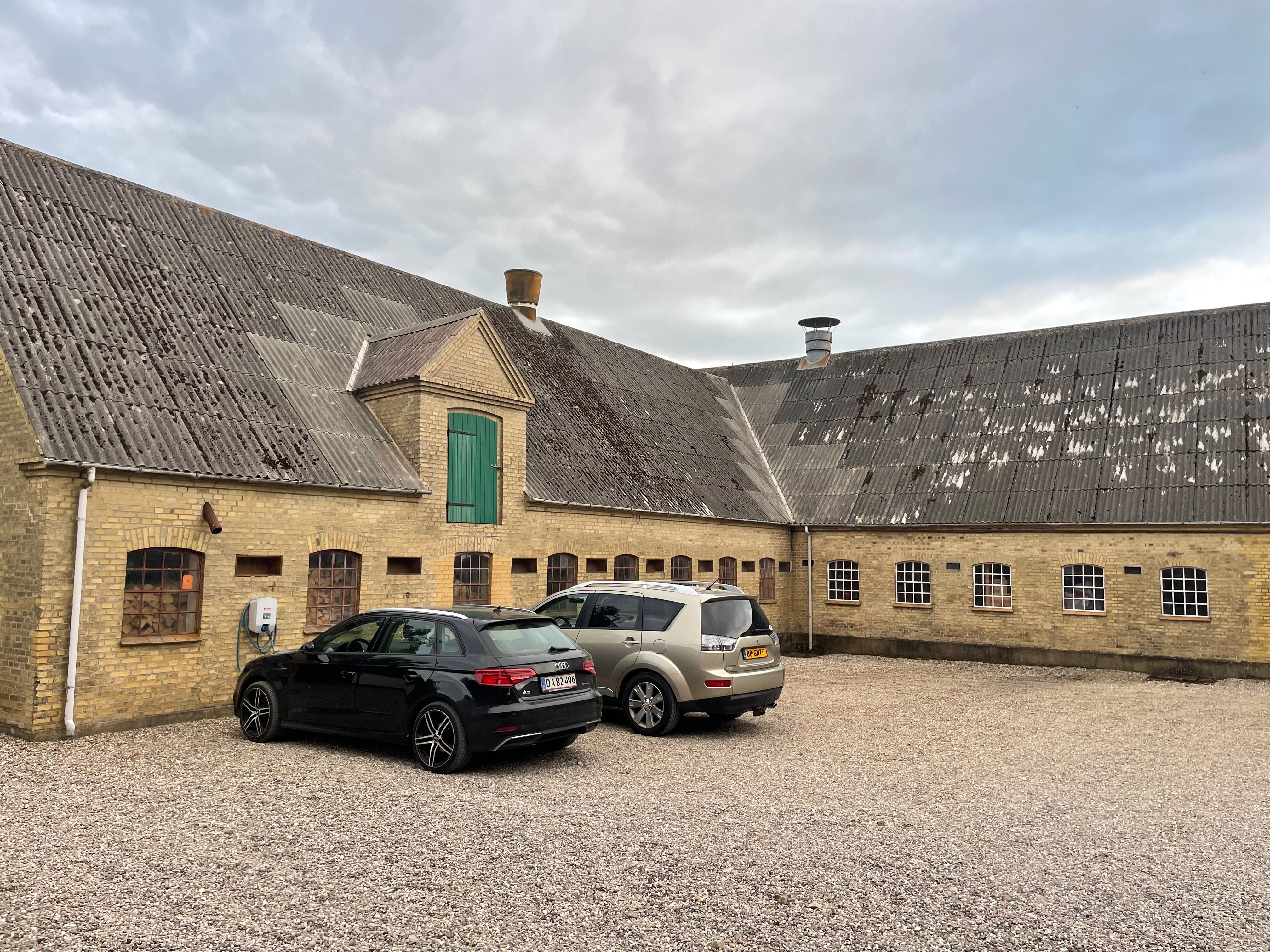 Annekset pa Langholm review showing the farm courtyard with old brick buildings parked cars gravel parking area and cloudy sky in Ringe Denmark
