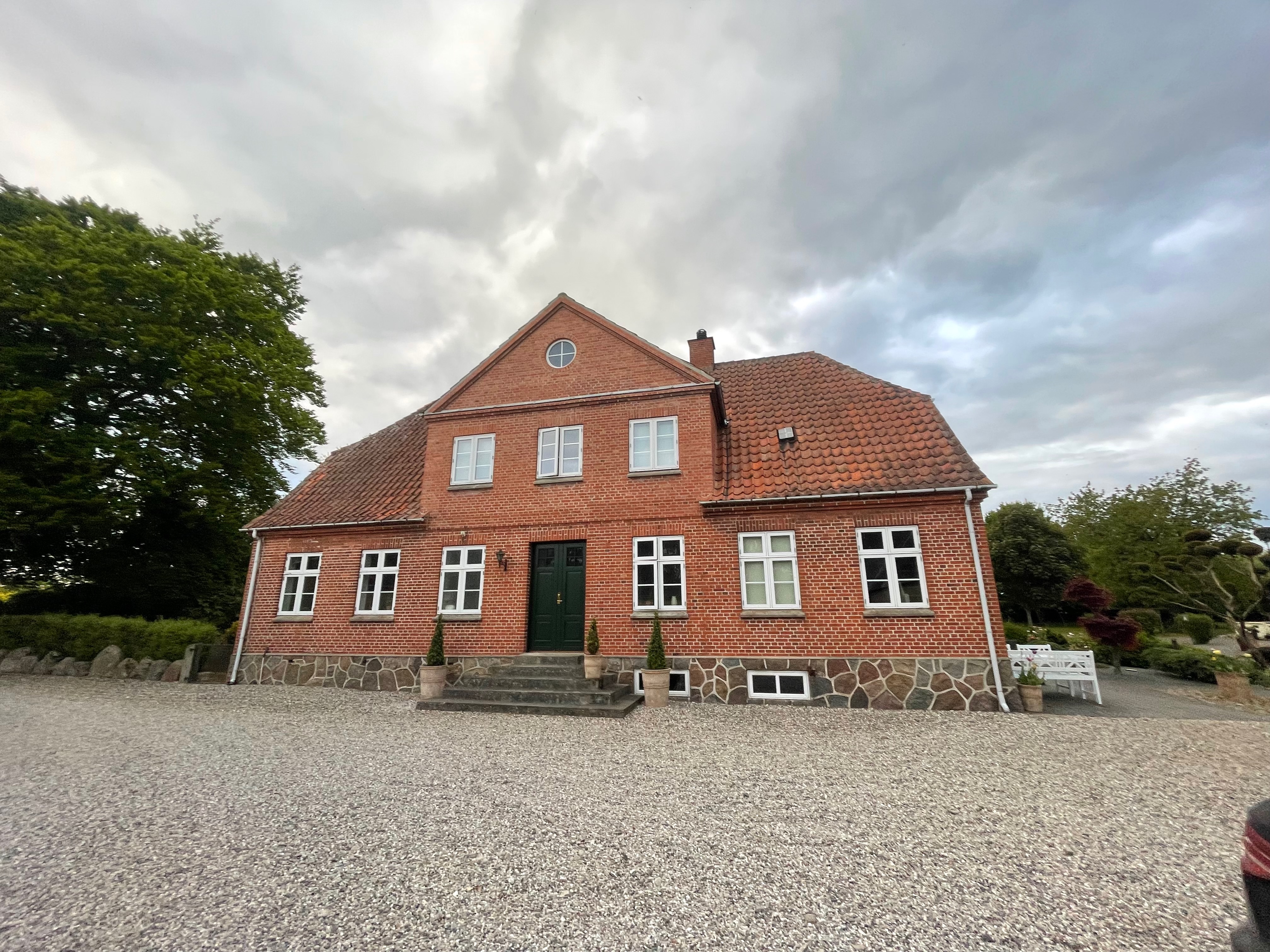 Annekset pa Langholm review showing the red brick farmhouse at the Airbnb property with gravel courtyard cloudy sky white windows green door and garden surroundings in Ringe Denmark