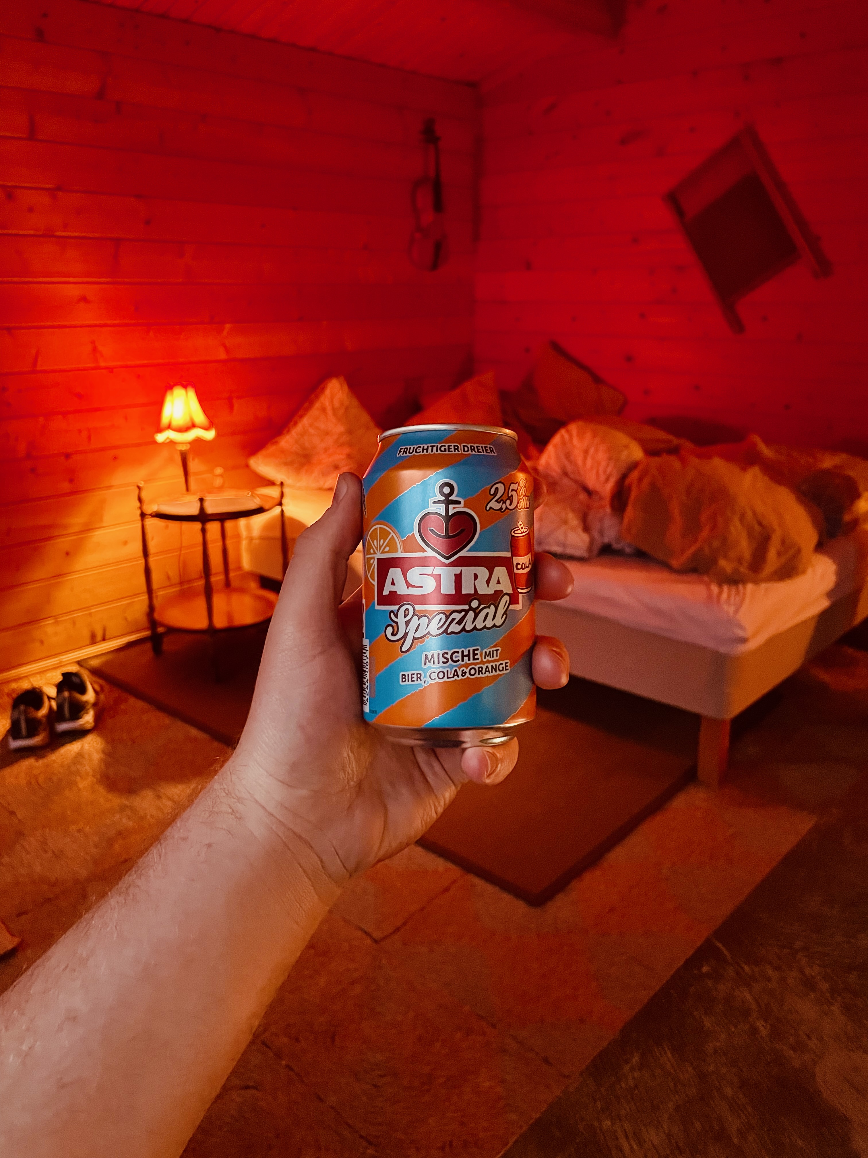 Annekset pa Langholm review showing an Astra Spezial drink held inside the cozy wooden Airbnb hut with red lighting wooden walls bed and warm evening atmosphere in Ringe Denmark
