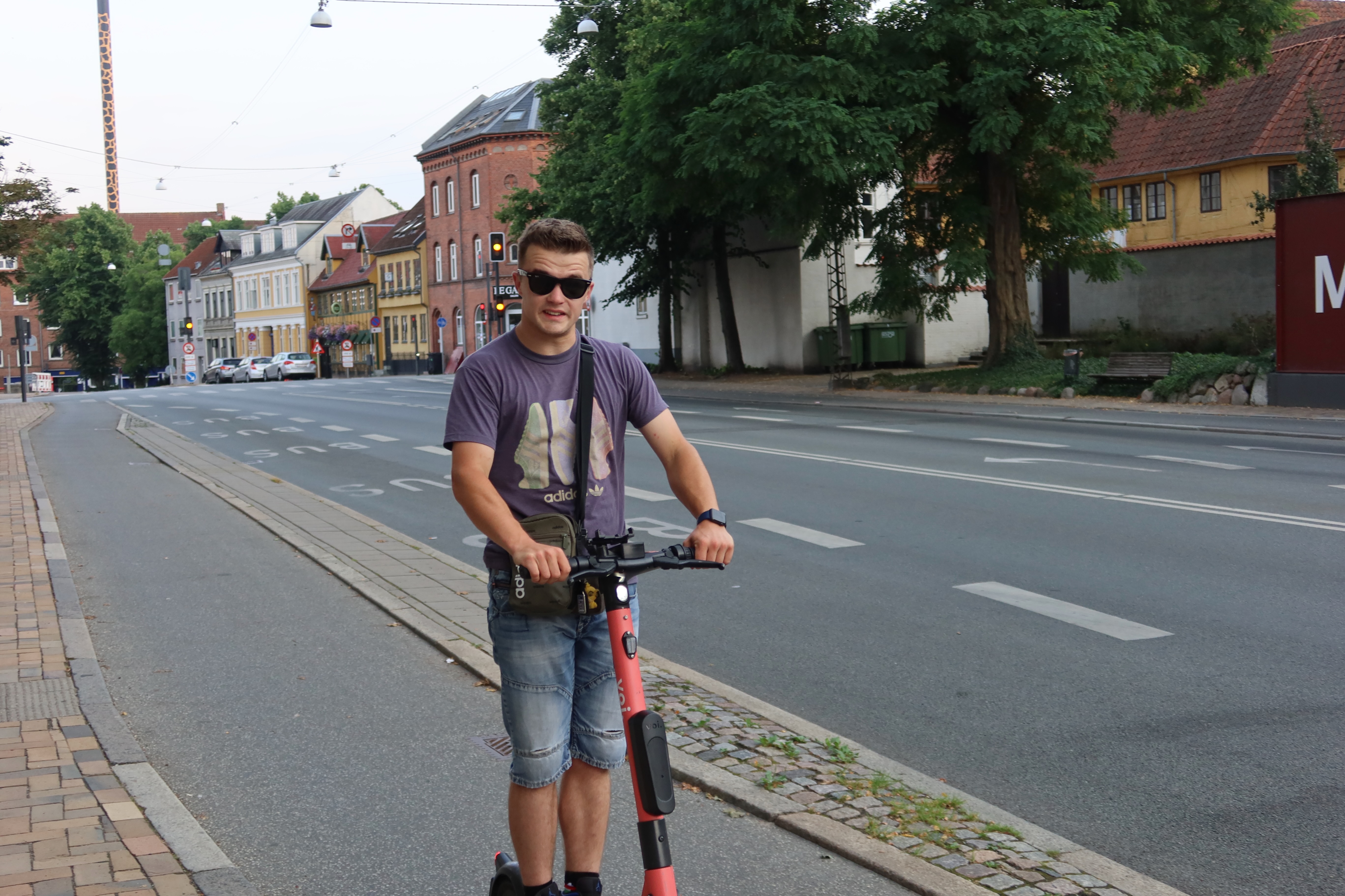 Voi Scooters Odense with Peter Smit riding a red shared electric scooter through a quiet city street in Odense Denmark