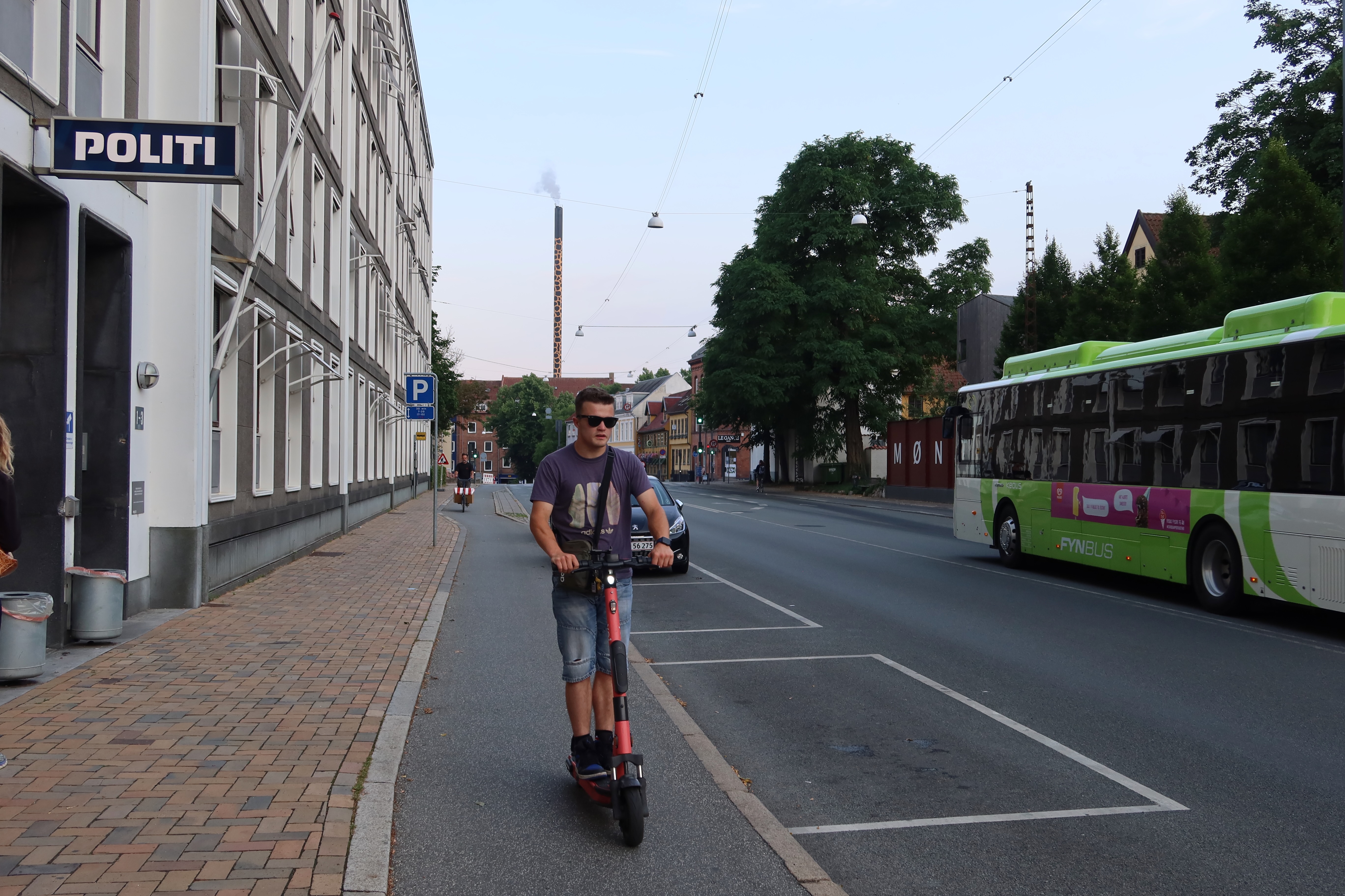 Voi Scooters Odense with Peter Smit riding a red shared electric scooter past the police station and city bus in Odense Denmark