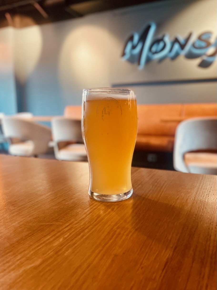 Mønsj Arendal beer served on a wooden table inside the cozy restaurant, with warm lighting, seating and the blurred Mønsj logo in the background in Arendal, Norway.