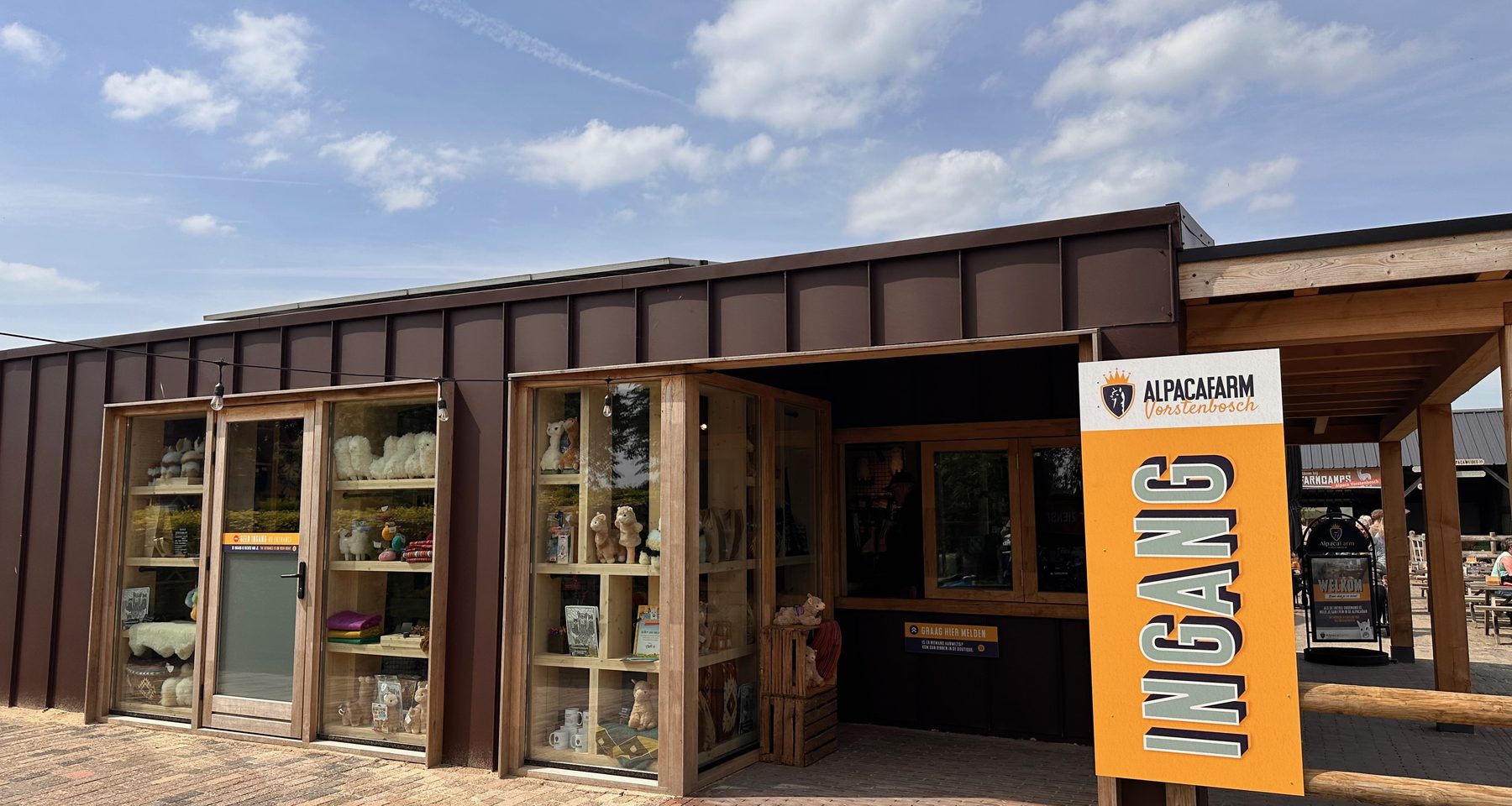 Alpacafarm Vorstenbosch review, entrance building with alpaca boutique, large orange welcome sign, and terrace area in North Brabant