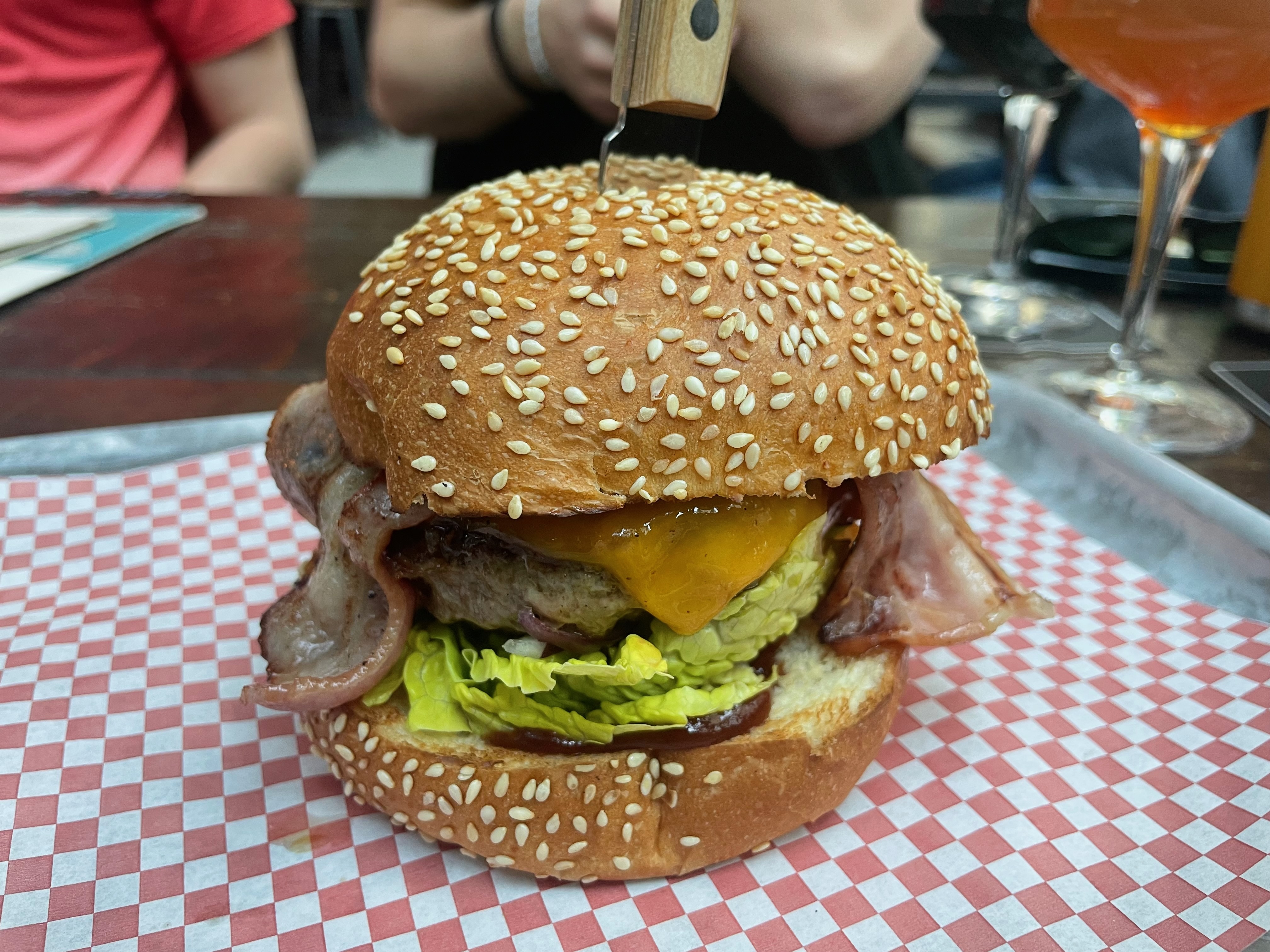BrewDog Outpost Rotterdam Review closeup of a bacon cheeseburger with sesame bun melted cheddar lettuce bacon and burger patty served on red checkered paper