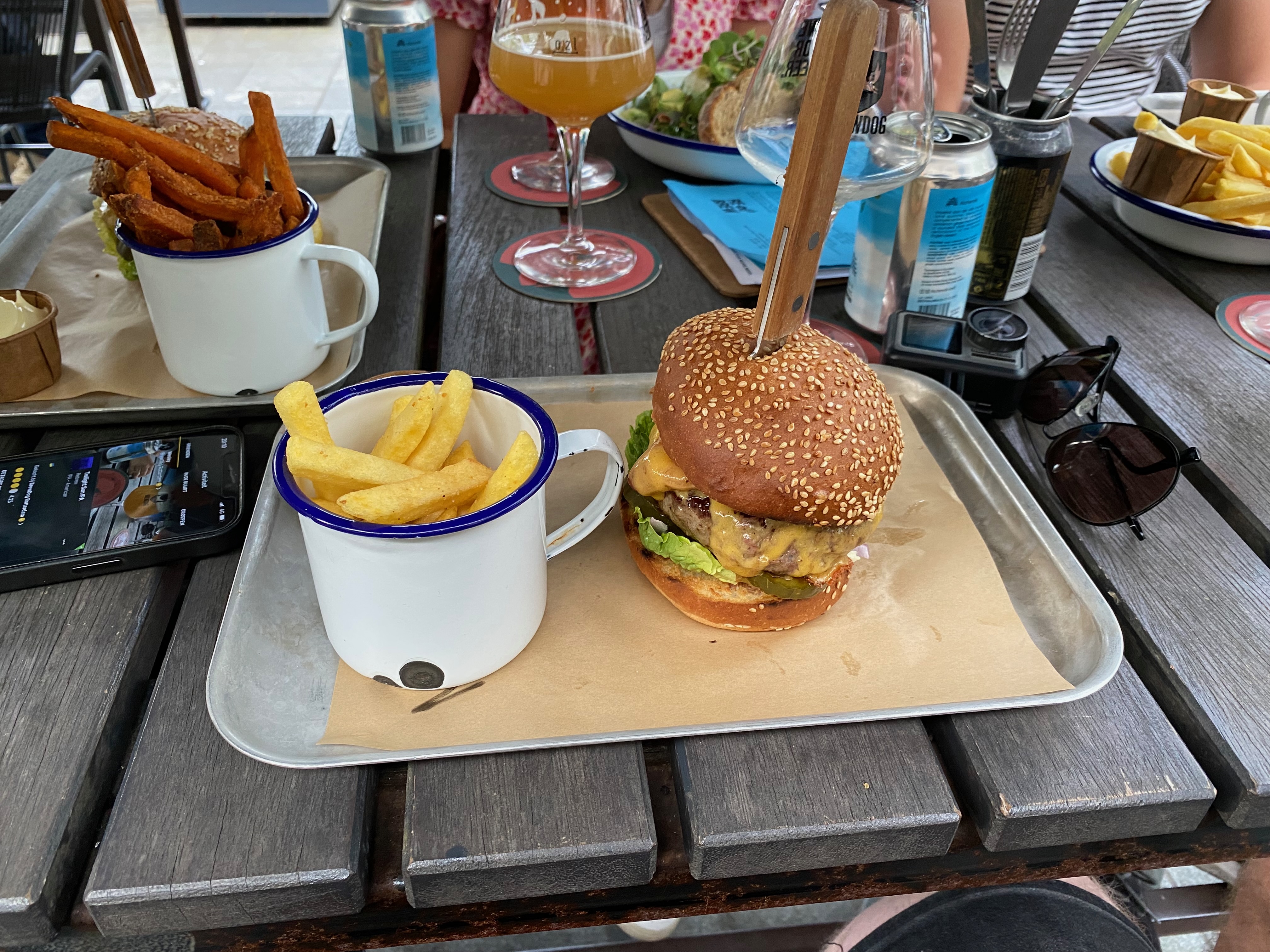 BrewDog Outpost Rotterdam Review with burger fries sweet potato fries craft beer glasses beer cans sunglasses and food trays on the terrace table