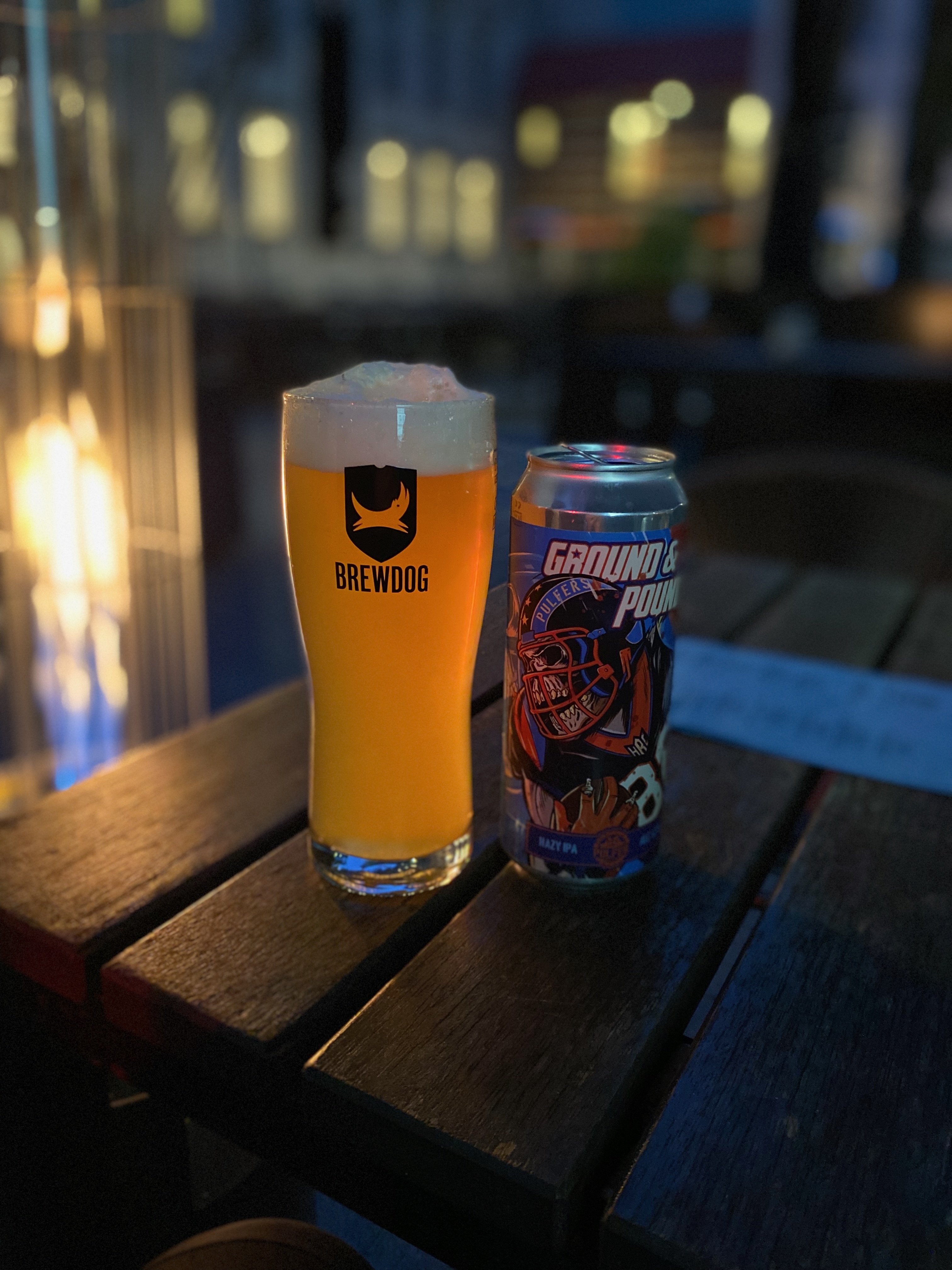 BrewDog Outpost Rotterdam Review with a BrewDog beer glass and Ground And Pound Hazy IPA can on a wooden table with warm evening pub lighting