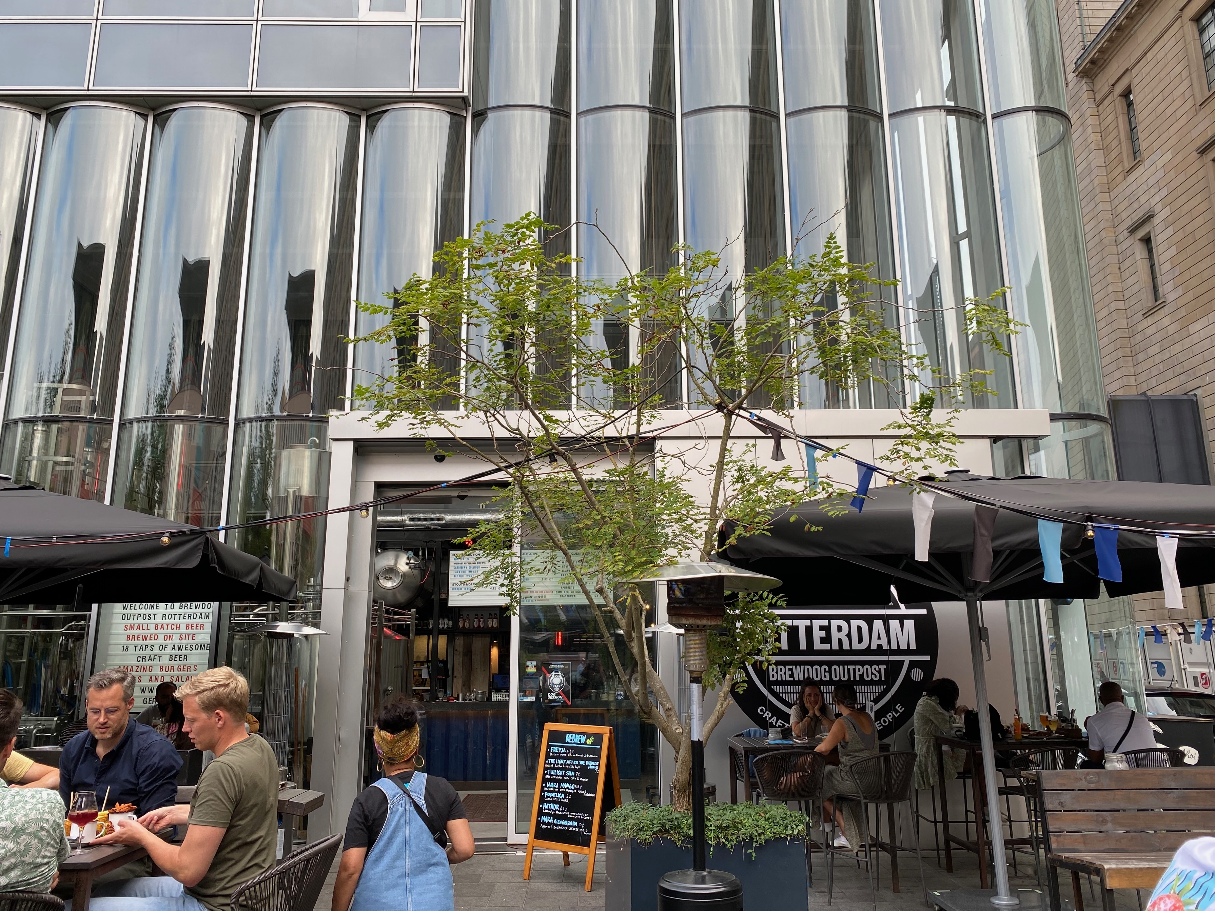 BrewDog Outpost Rotterdam Review showing the exterior terrace entrance glass facade BrewDog Outpost Rotterdam signage umbrellas and outdoor seating at Halvemaanpassage