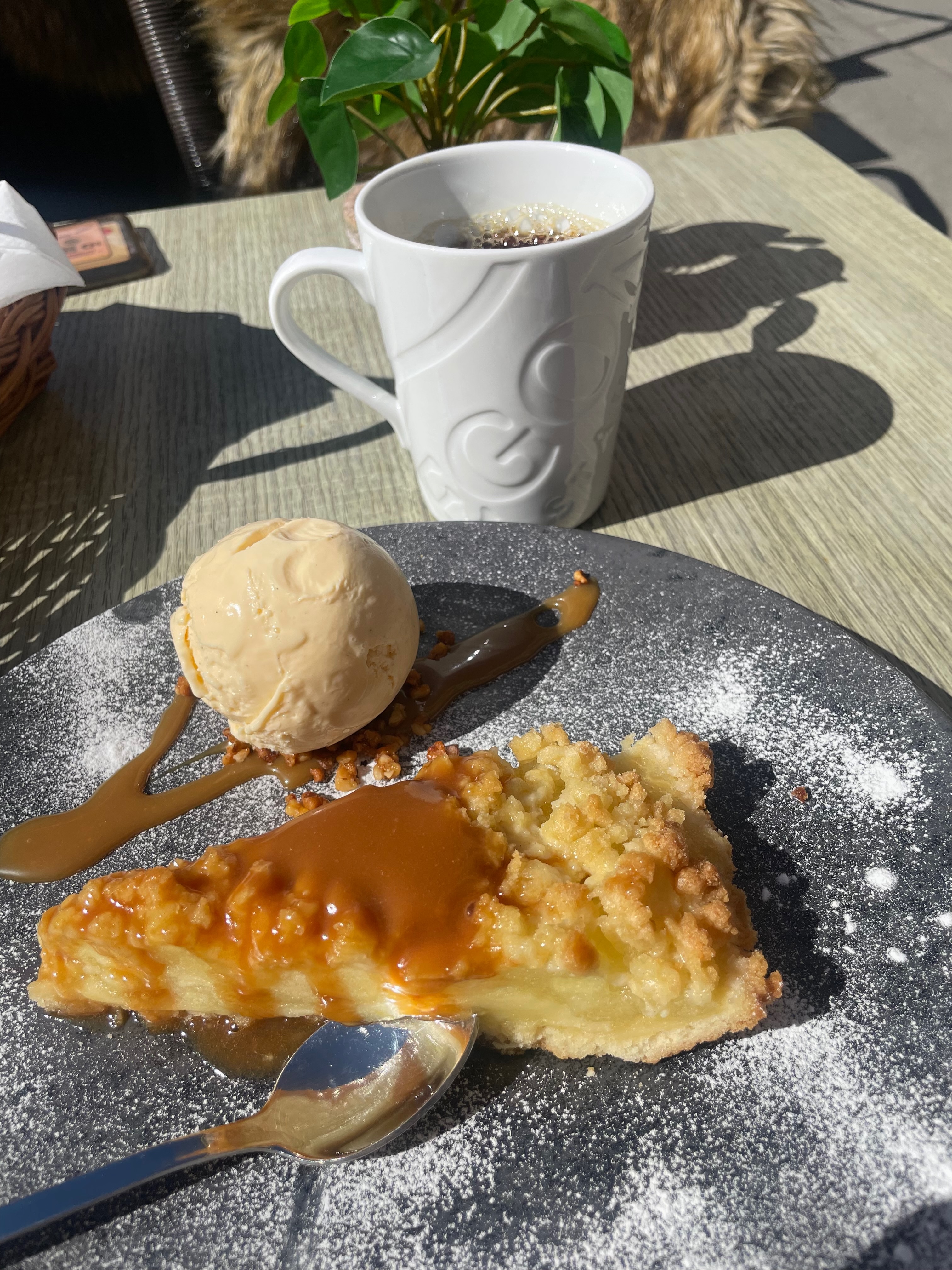 Warm apple cake with ice cream, caramel sauce, powdered sugar, and black coffee on the terrace at Egon Karl Johan in Oslo.