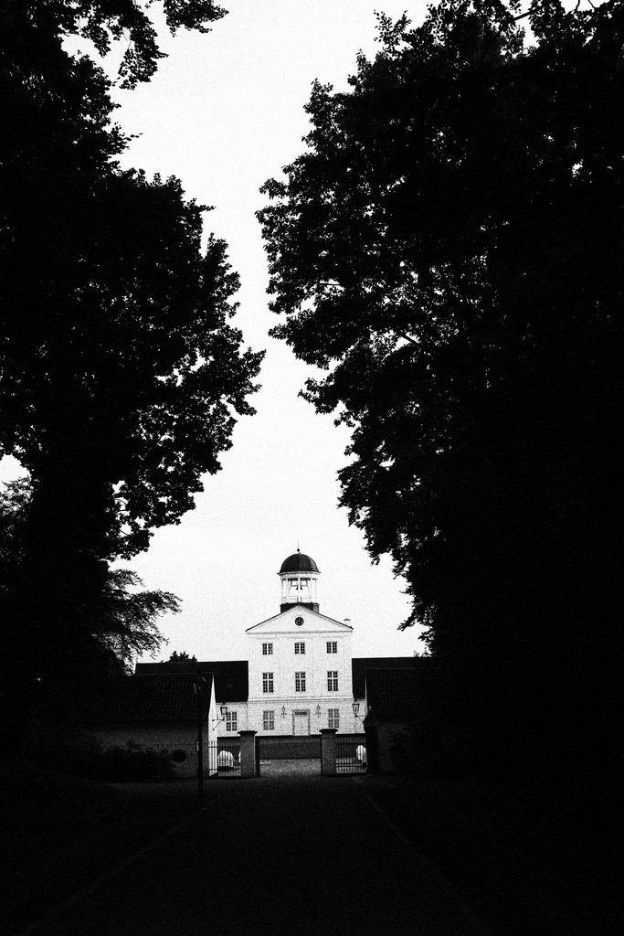 Gråsten Slot in black and white, showing the royal palace entrance framed by dark trees and the central tower.