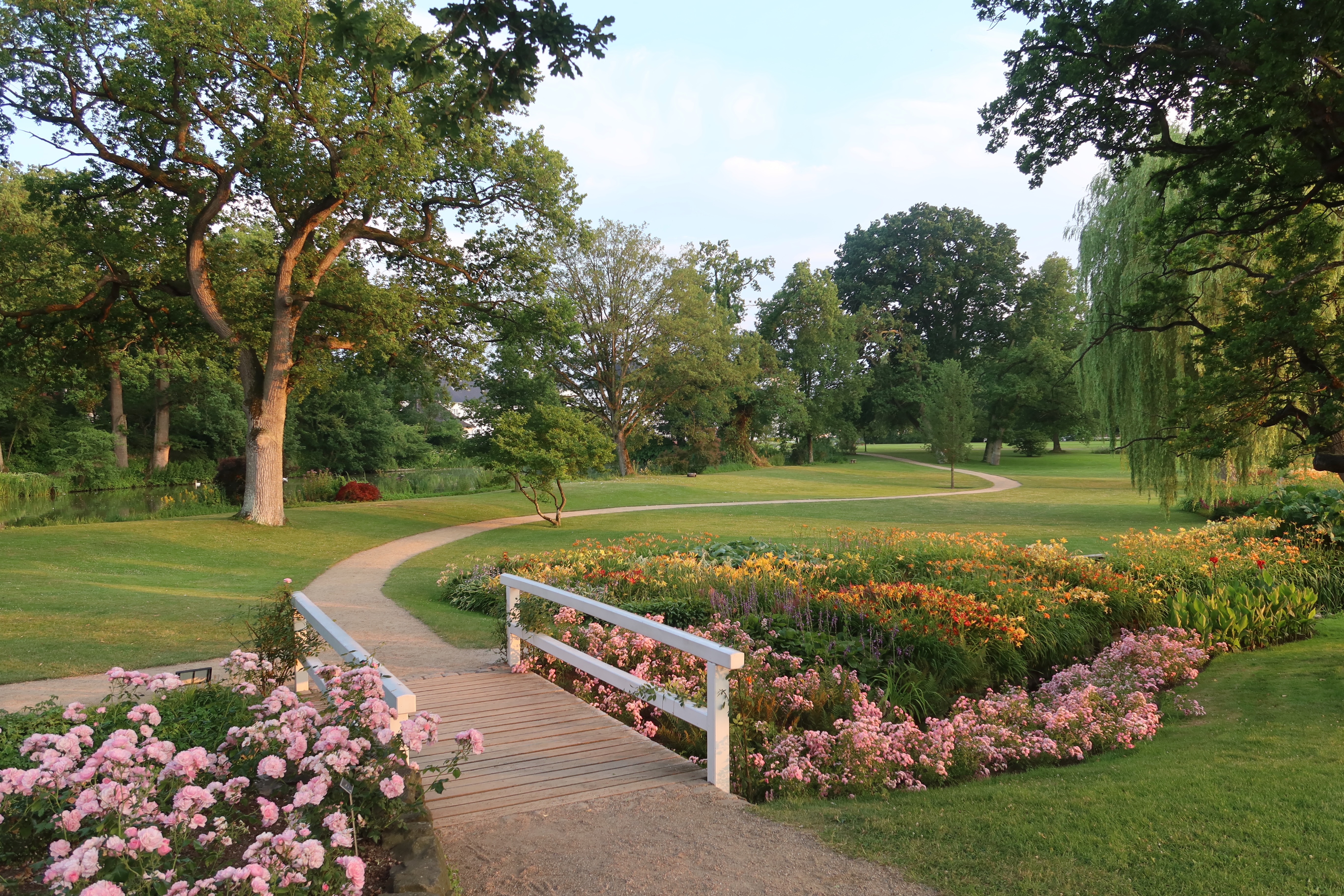Gråsten Slot palace garden with a small white bridge, colorful flower beds, walking path, and peaceful park landscape.