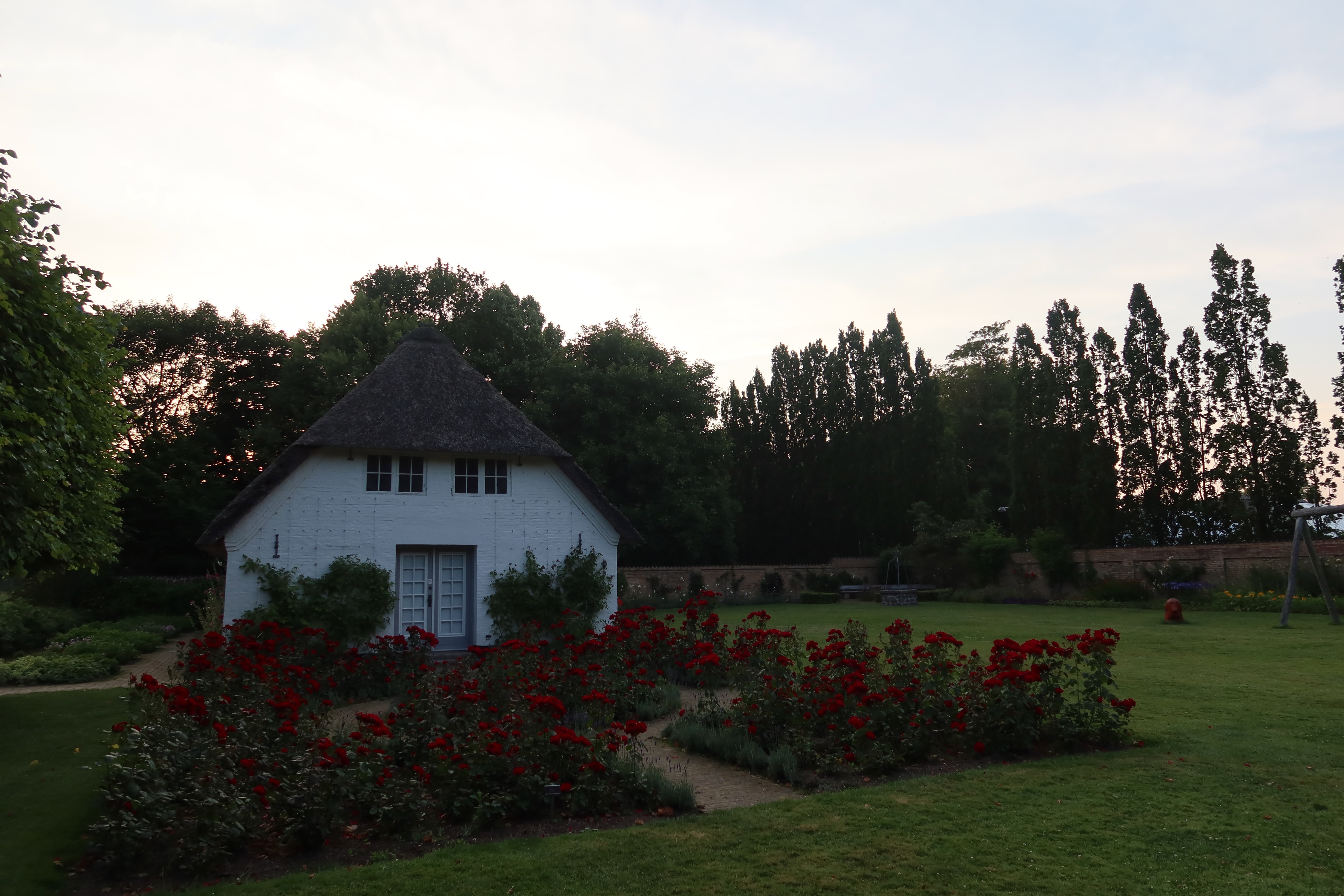 Gråsten Slot palace garden with a white thatched garden cottage, red roses, green lawn, and trees in Southern Denmark.
