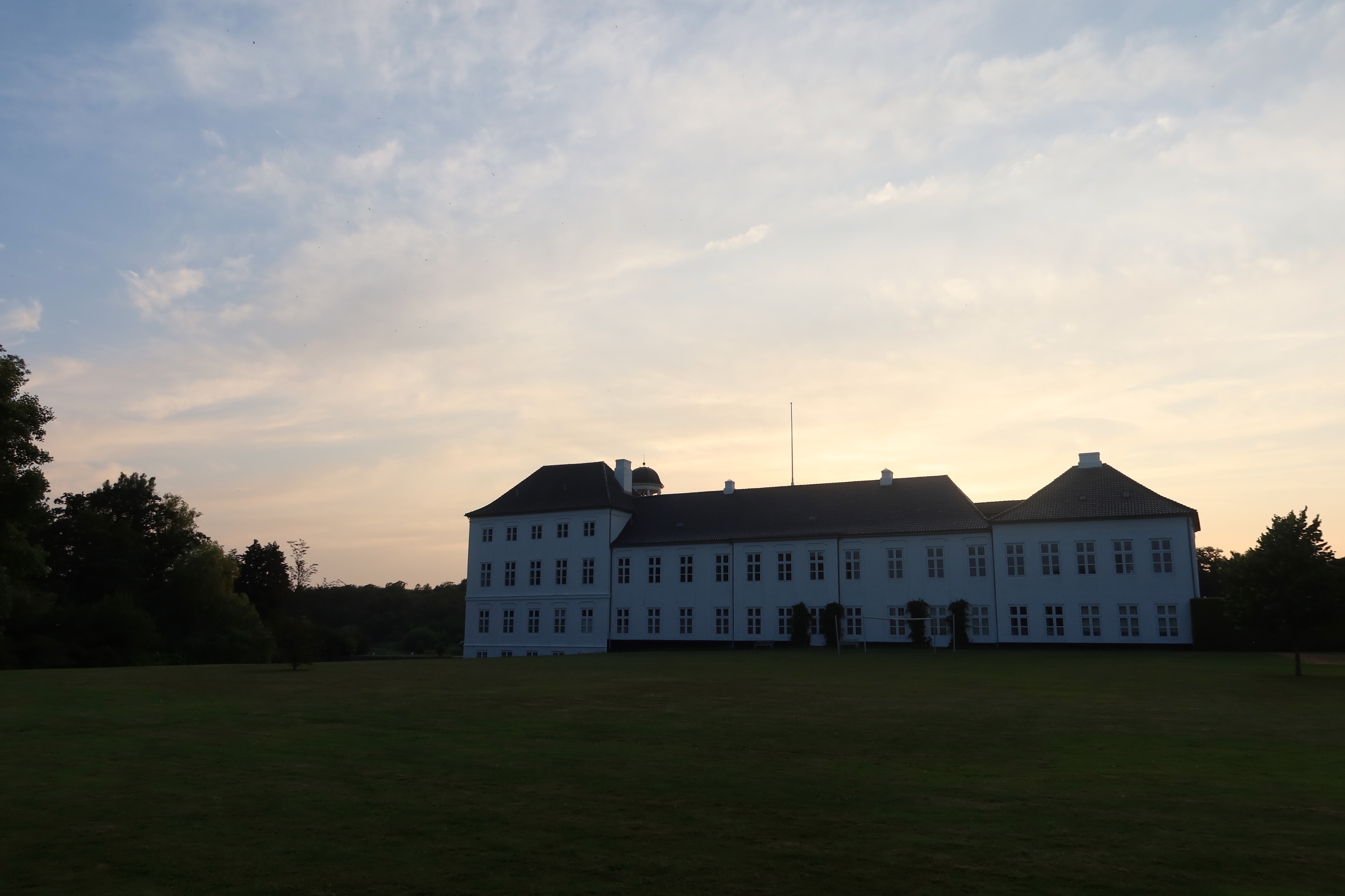 Gråsten Slot seen from the palace garden at sunset, with the white royal residence, open lawn, and soft evening sky in Southern Denmark.