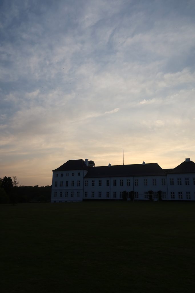 Gråsten Slot seen from the palace garden at sunset, with the royal palace in silhouette under a dramatic evening sky in Southern Denmark.