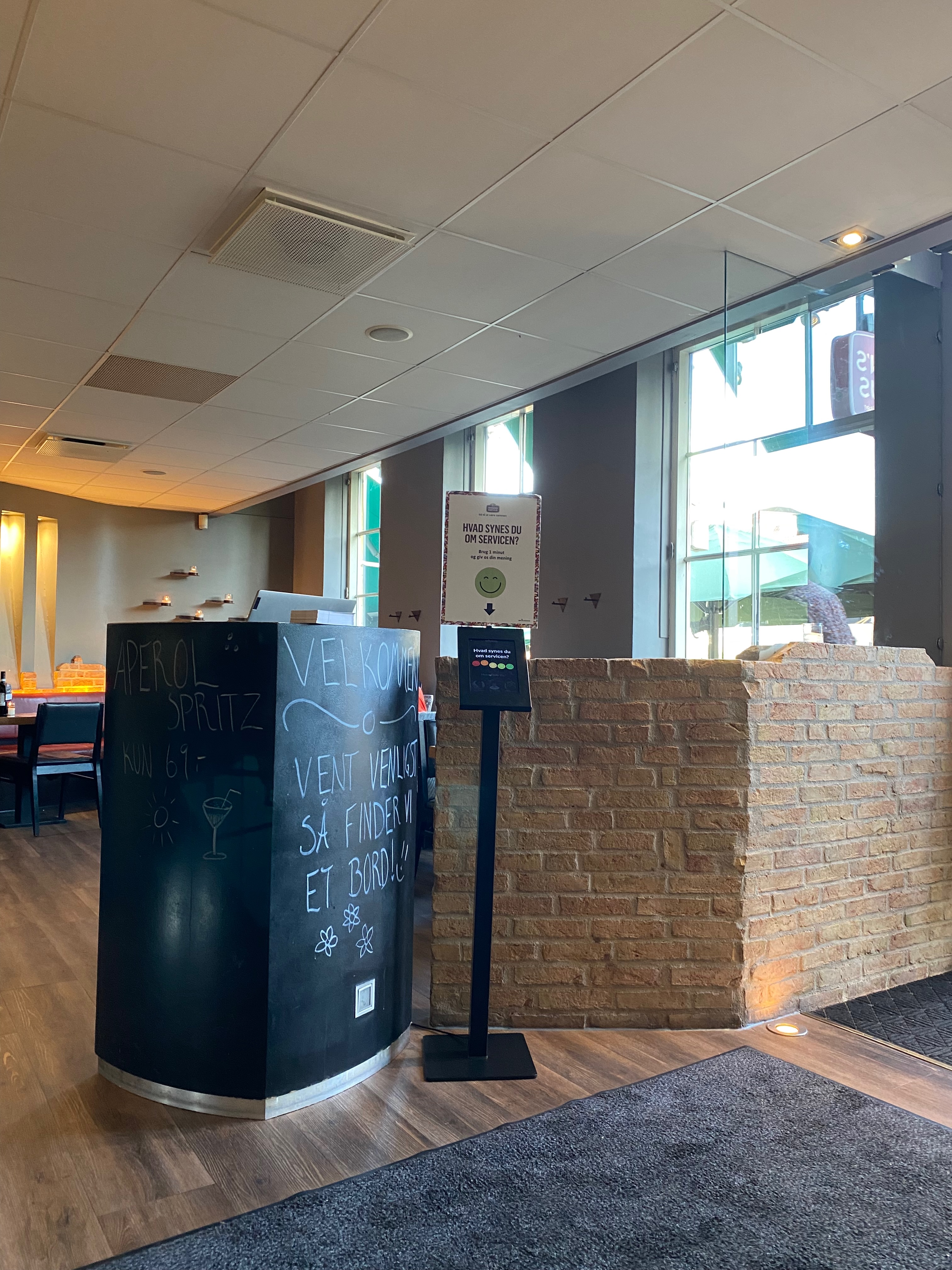 Jensens Bofhus Silkeborg review showing the entrance area inside the former restaurant in Silkeborg Denmark with chalkboard signs brick walls large windows and a service feedback stand