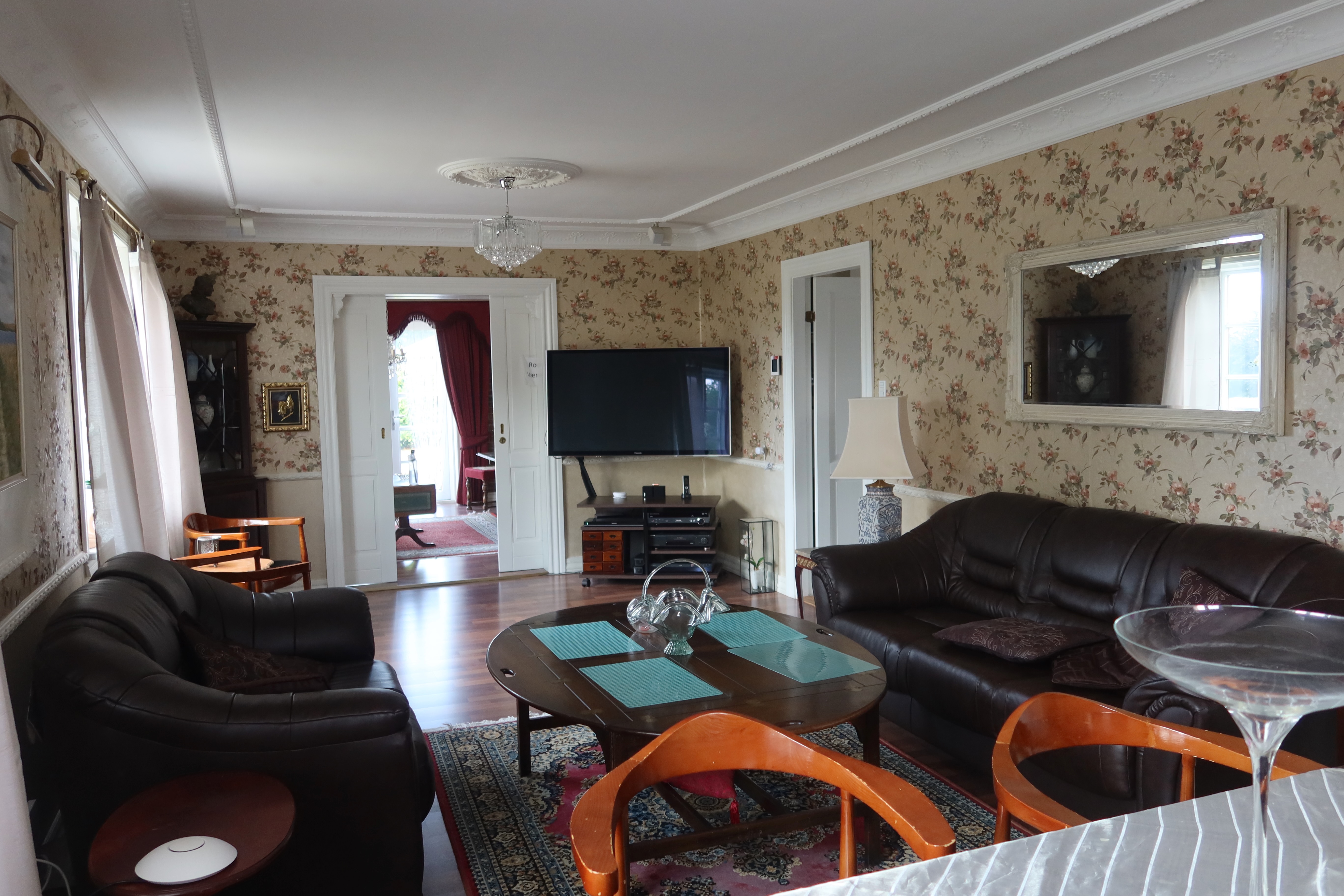 Kollund Rooms Review IMG 2601 showing a shared guest lounge with leather sofas, television, floral wallpaper, mirror, wooden table, and old fashioned interior details at Kollund Rooms.