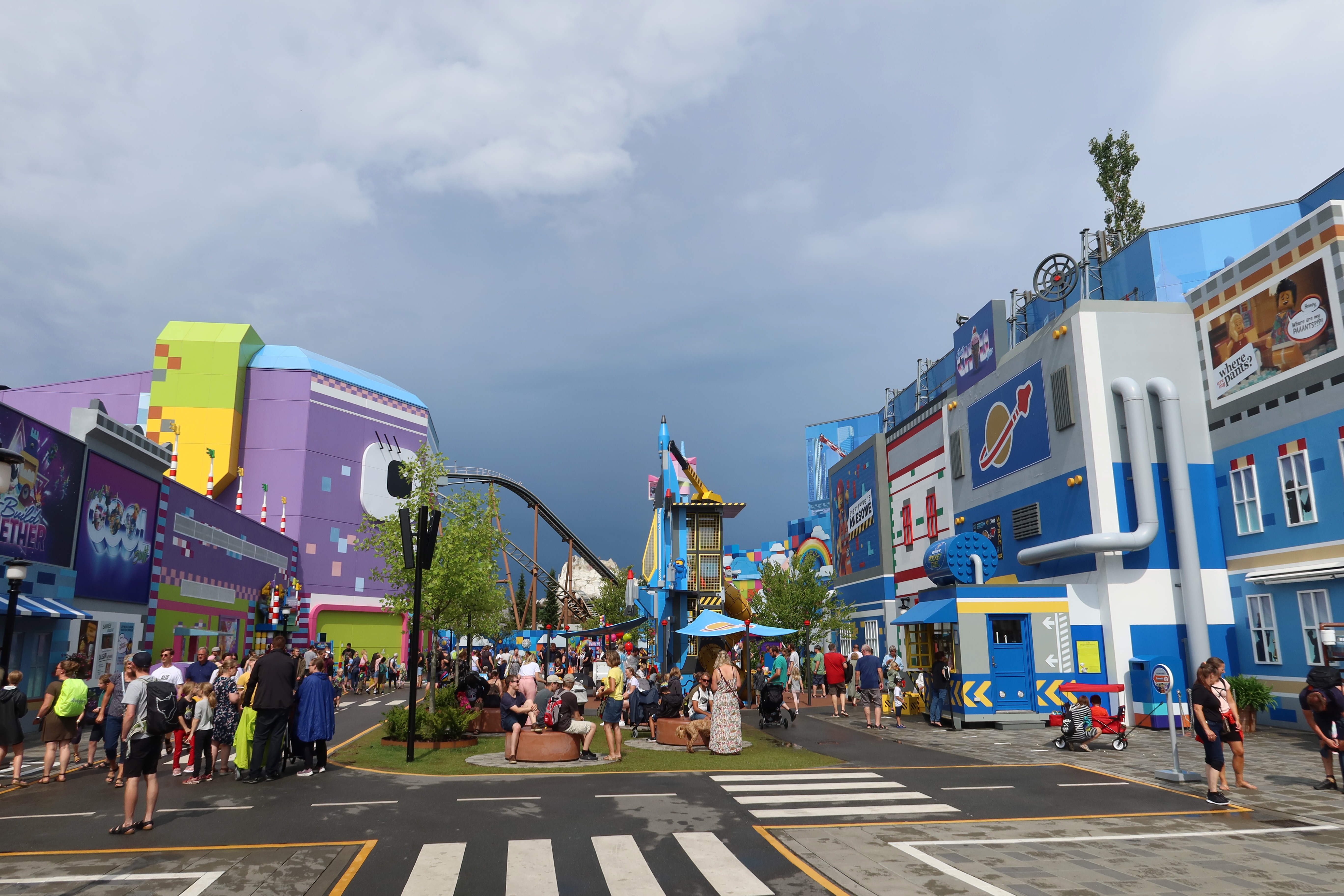 LEGOLAND Billund review IMG 2786 showing the colorful LEGO Movie World area with themed buildings coaster track visitors and dramatic cloudy sky at LEGOLAND Billund Denmark