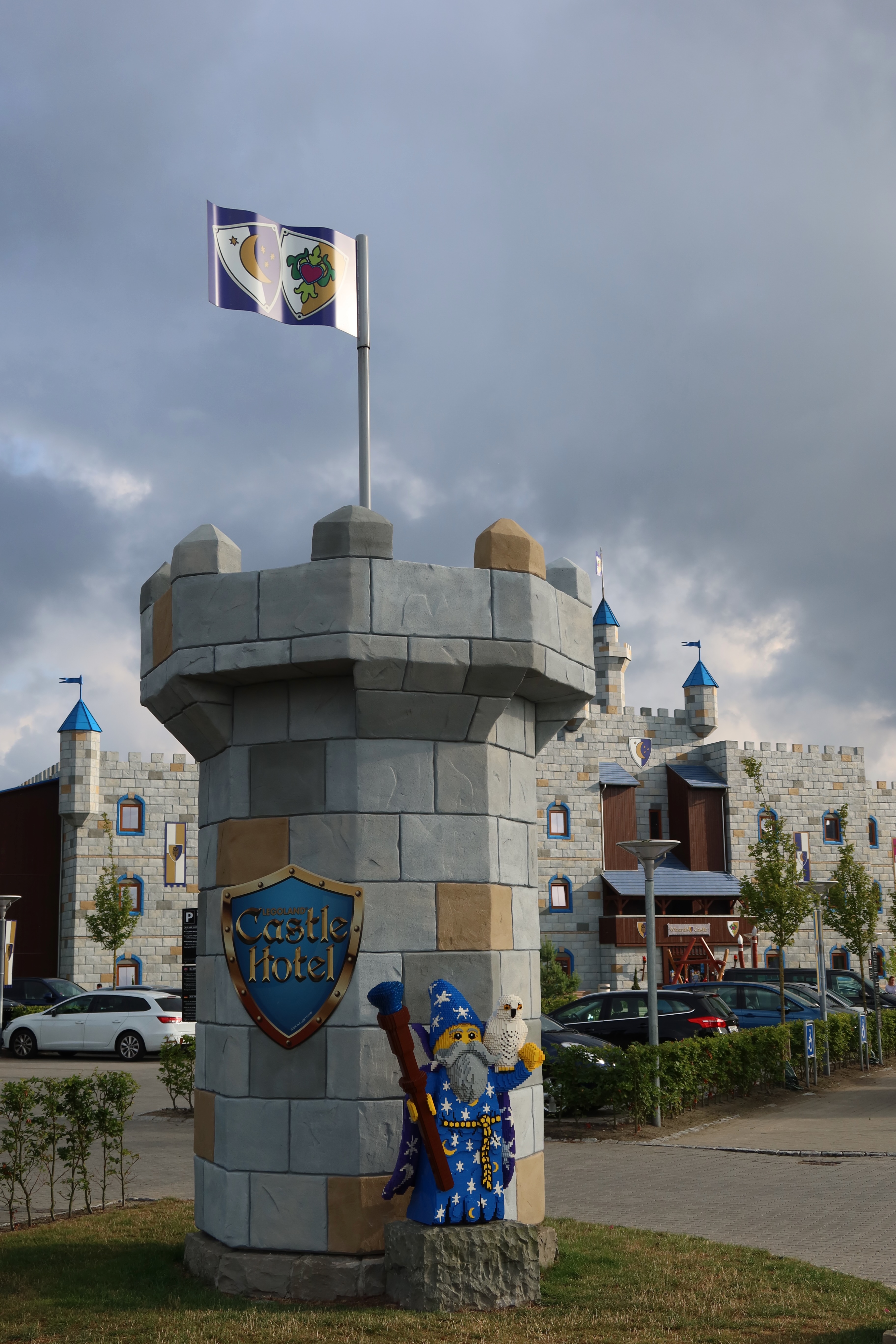 LEGOLAND Castle Hotel IMG 2881 showing the castle tower sign with a LEGO wizard figure flags parked cars and the hotel building at LEGOLAND Billund Resort in Denmark