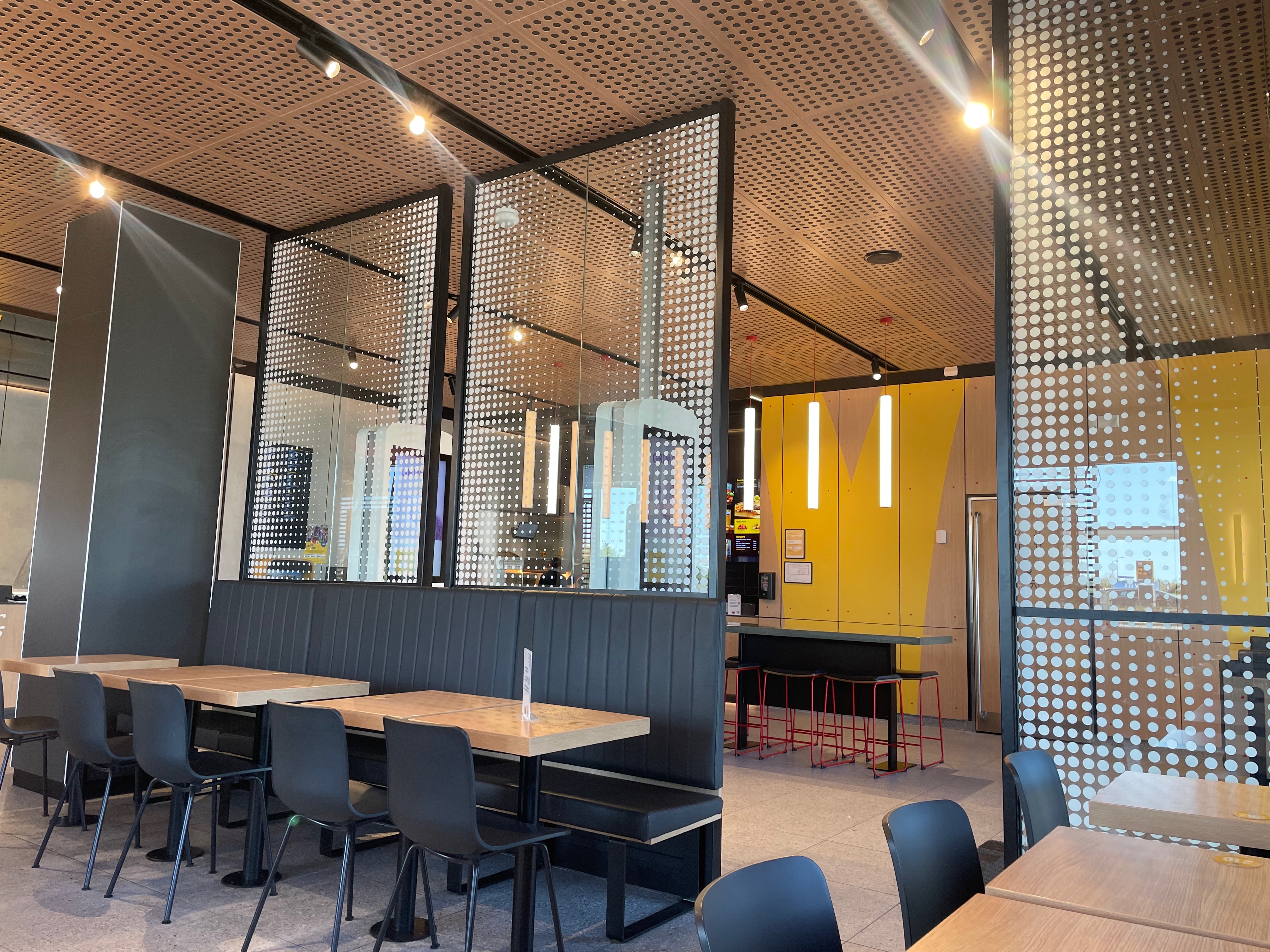 McDonald's Brønderslev interior with modern seating, glass dividers, wooden ceiling panels, yellow wall details and table service area in Denmark
