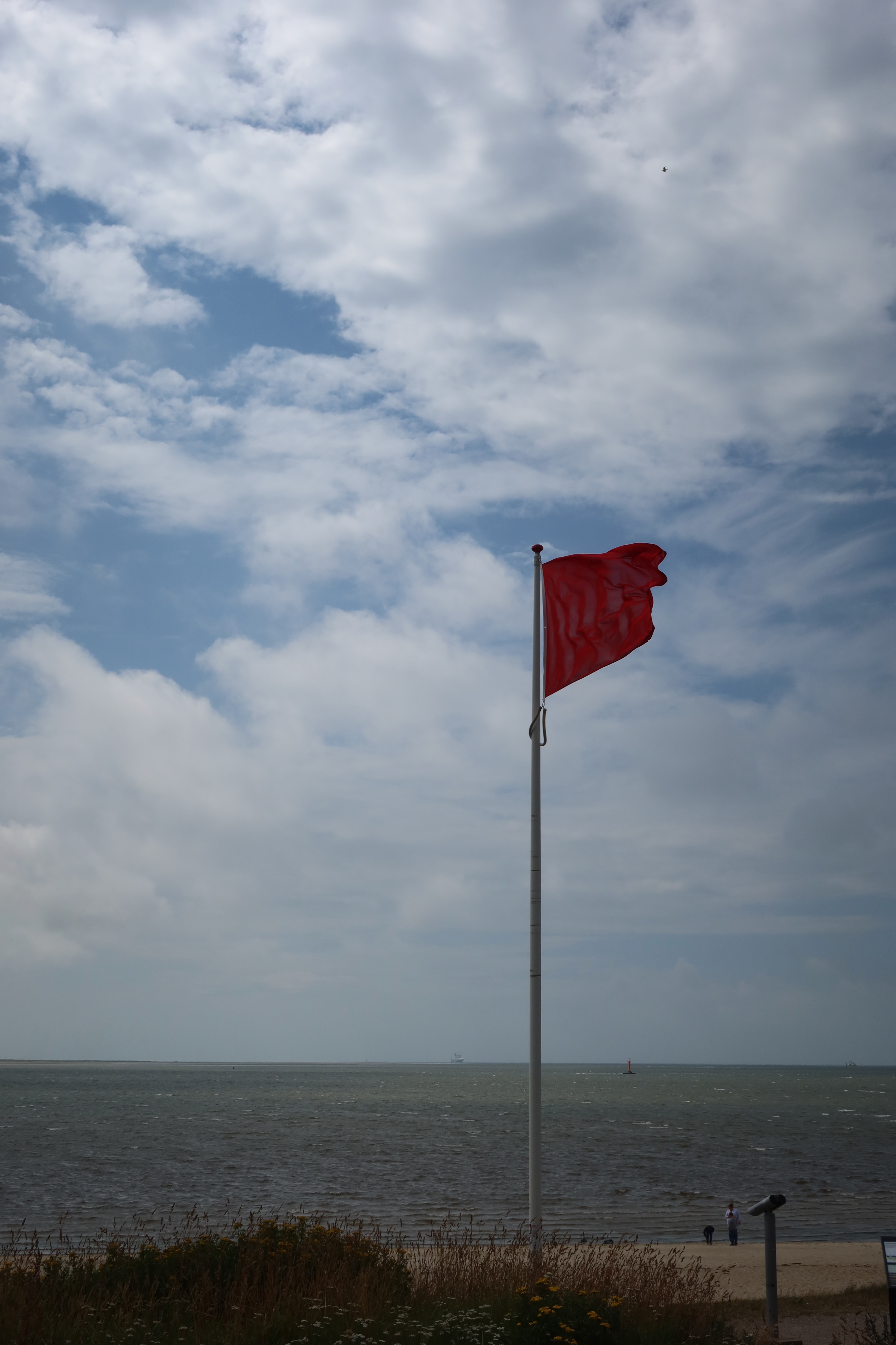 Mennesket ved Havet coastal area in Esbjerg Denmark with a red beach flag and cloudy sky over the sea