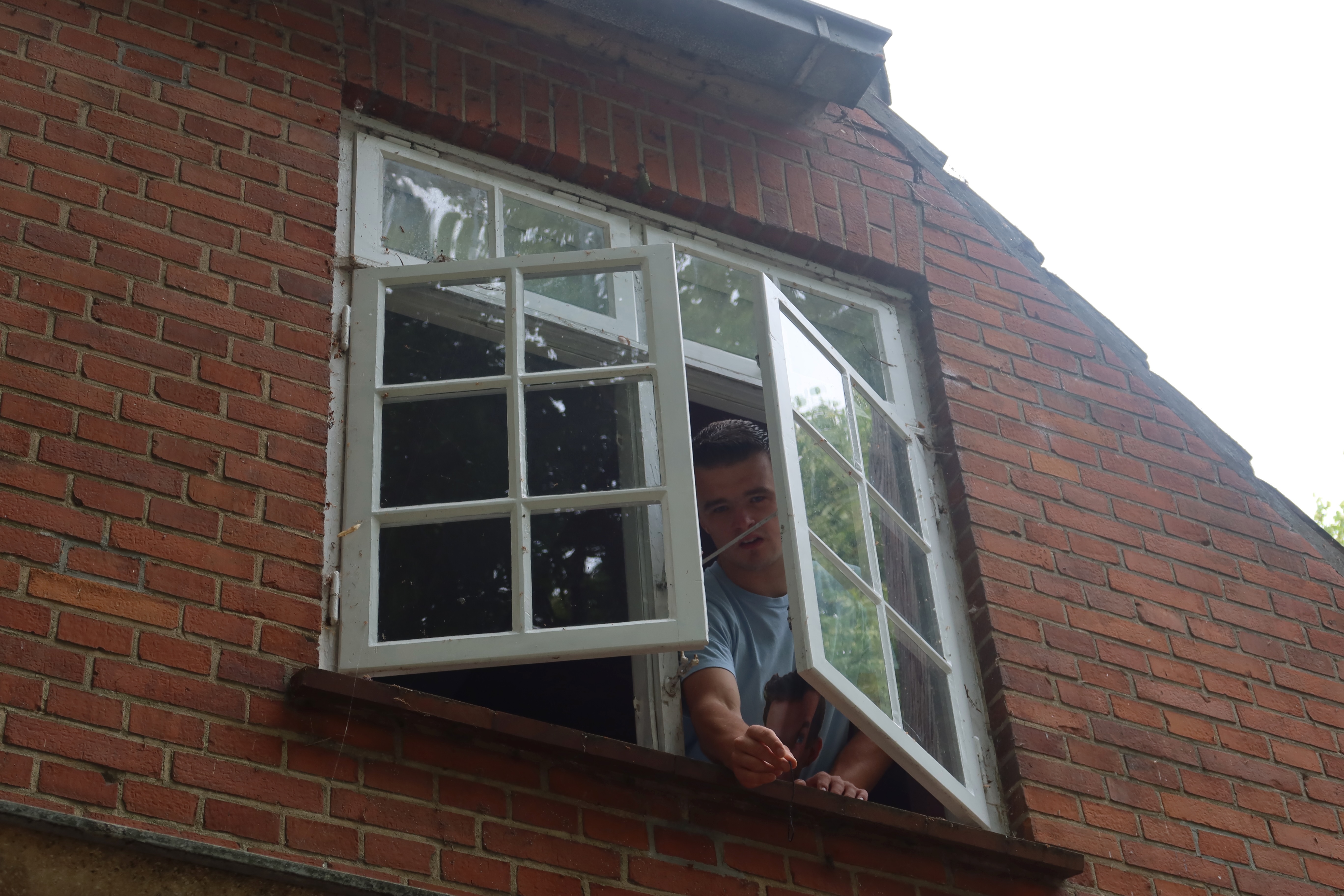 Mjelsgaard 1 Airbnb Review showing Peter Smit looking out from the upstairs window of the red brick Airbnb house in Denmark, with old white window frames and countryside character