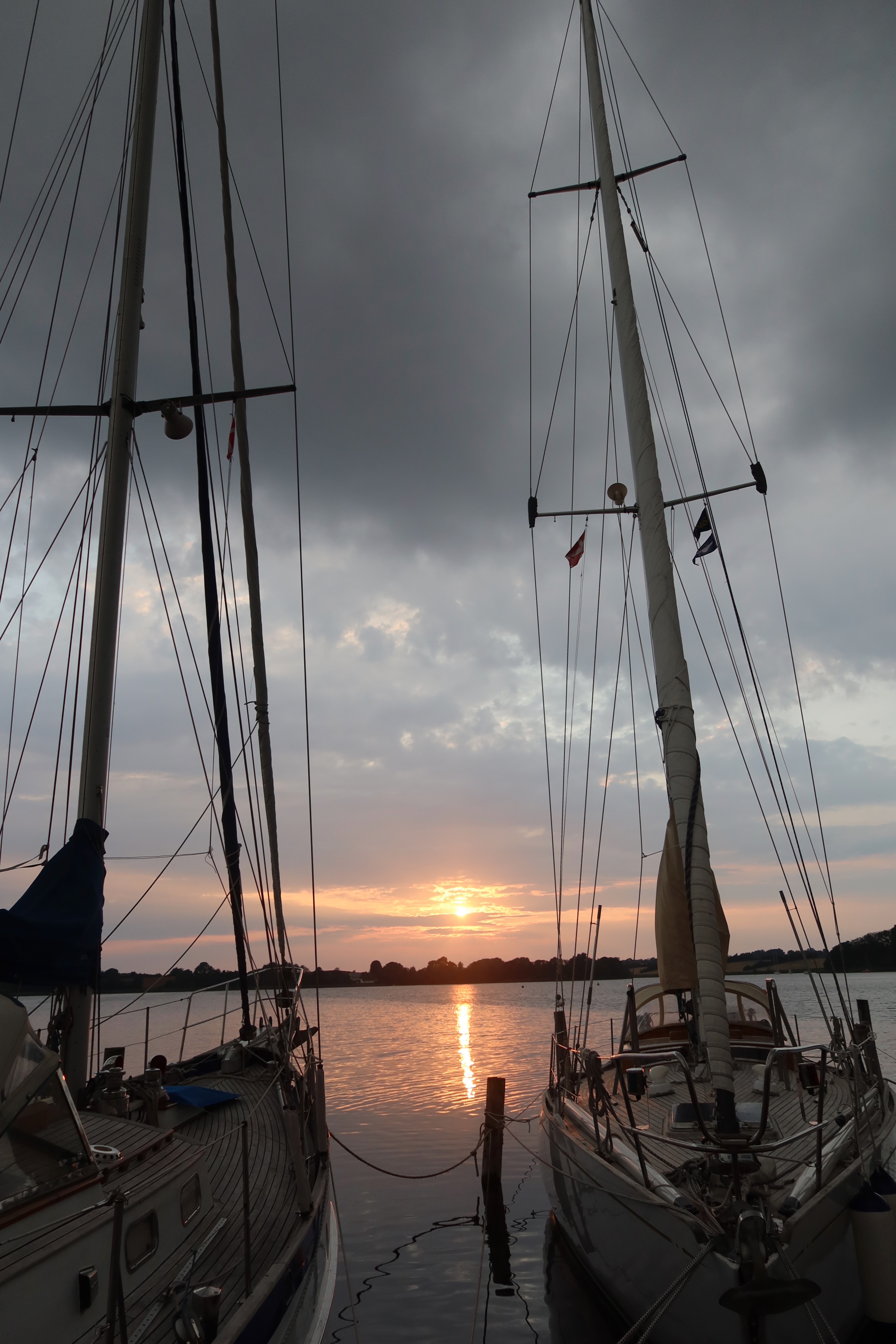 Mjelsvig Harbor sunset between sailboats with calm water and dark clouds in Mjels Denmark