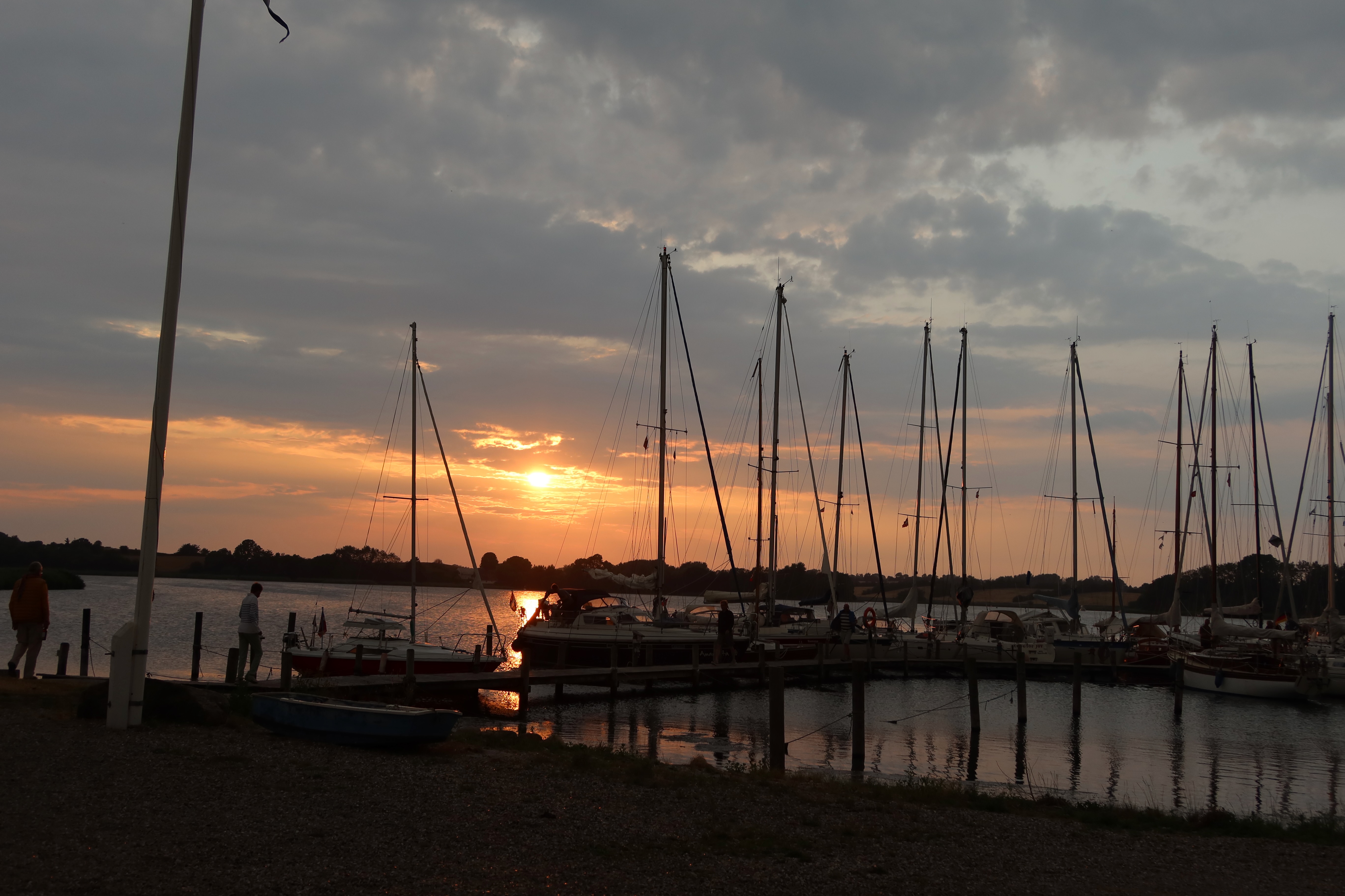 Mjelsvig Harbor at sunset with sailboats, calm marina water, dramatic clouds, and warm orange light in Mjels Denmark