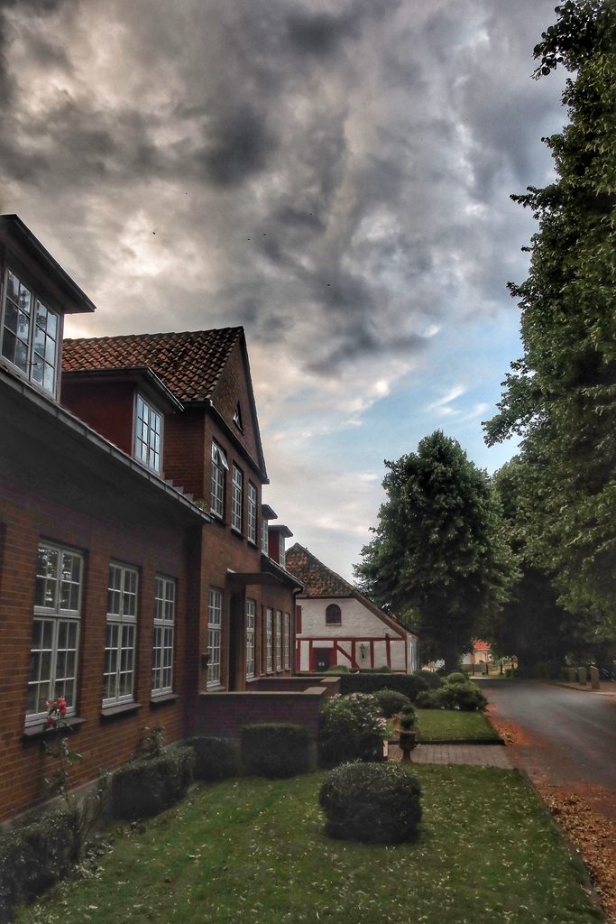 Mjelsvig Harbor area with a quiet village street, traditional brick houses, trees, and dramatic storm clouds in Mjels Denmark