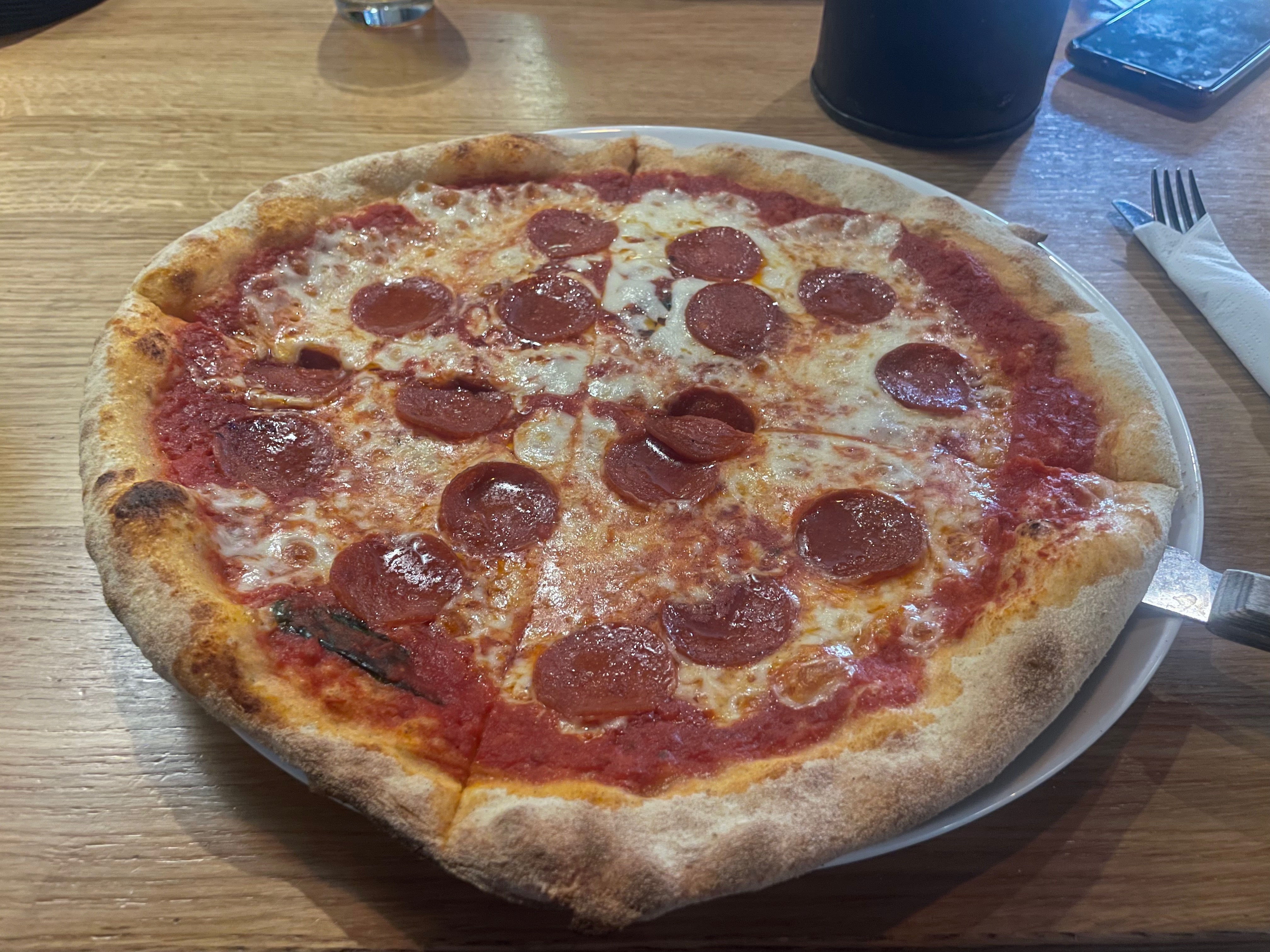 Mønsj Arendal salami pizza served on a wooden table, with melted cheese, tomato sauce, spicy salami and a thin crispy crust in Arendal, Norway.