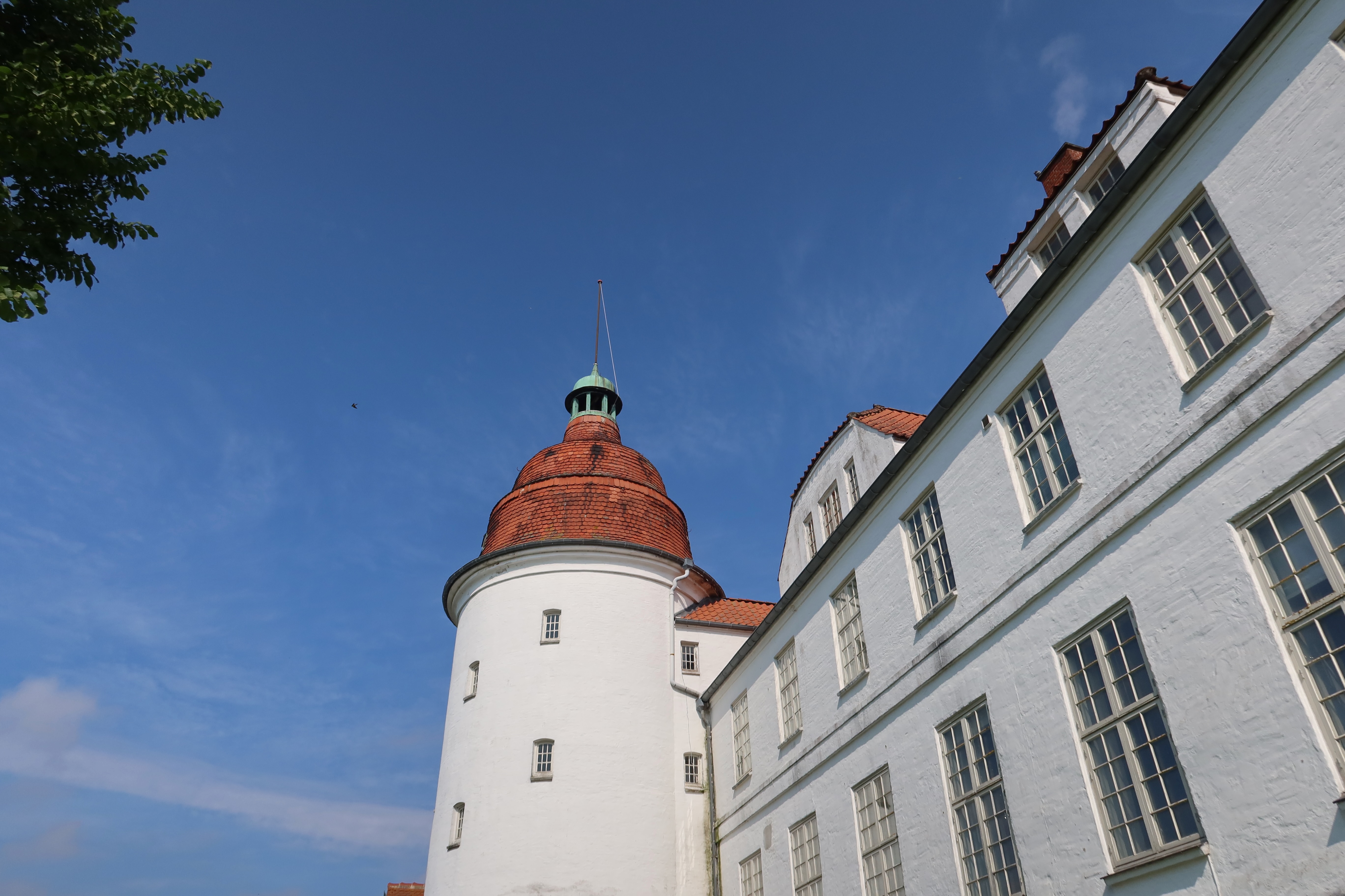 Nordborg Slot white tower and castle wall with red tiled roof under a clear blue sky in Nordborg Denmark