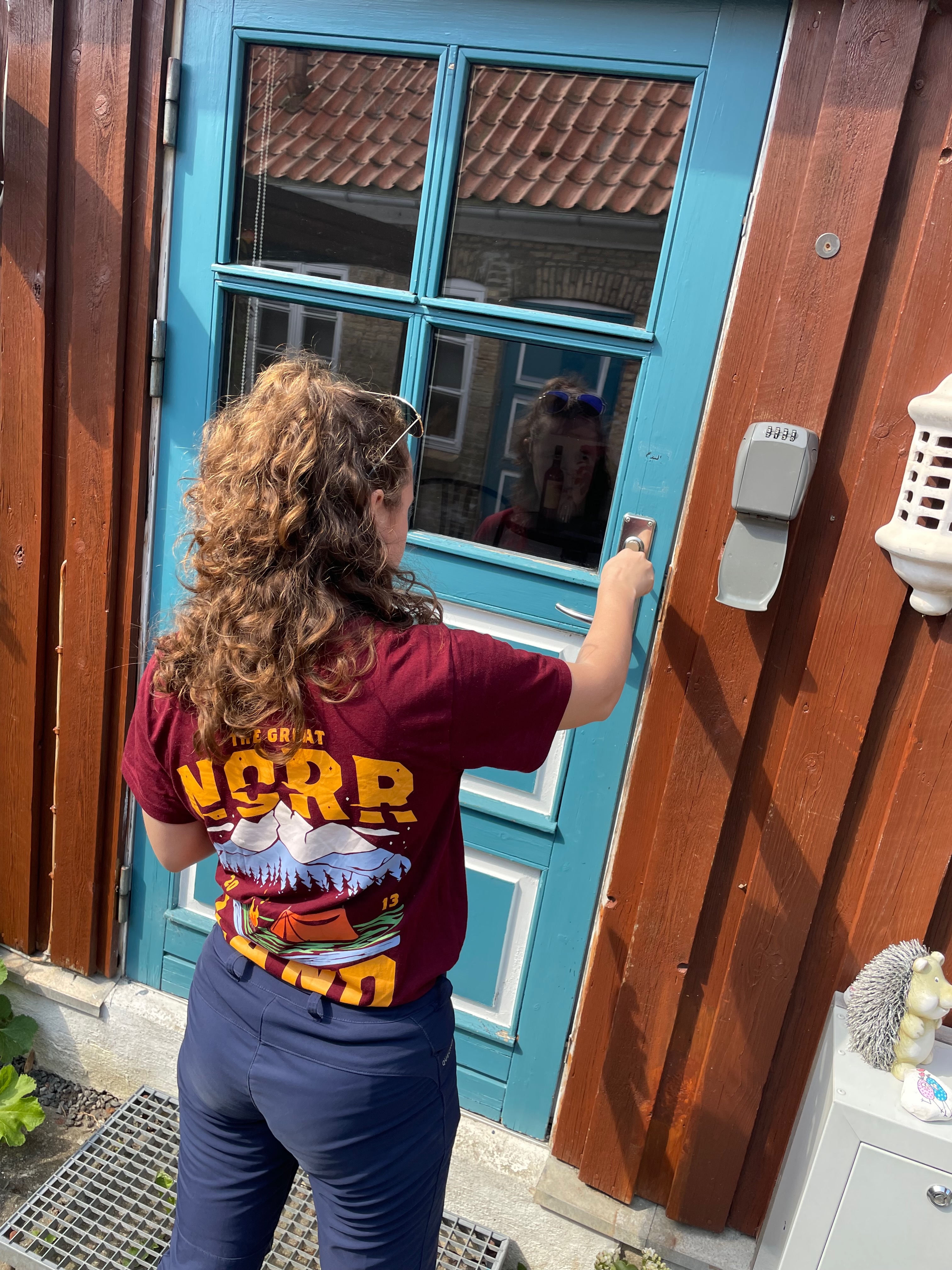 Private Annex Haderslev Review showing a guest checking in at the blue Airbnb door in Haderslev, with the key box, wooden annex wall and courtyard entrance visible.