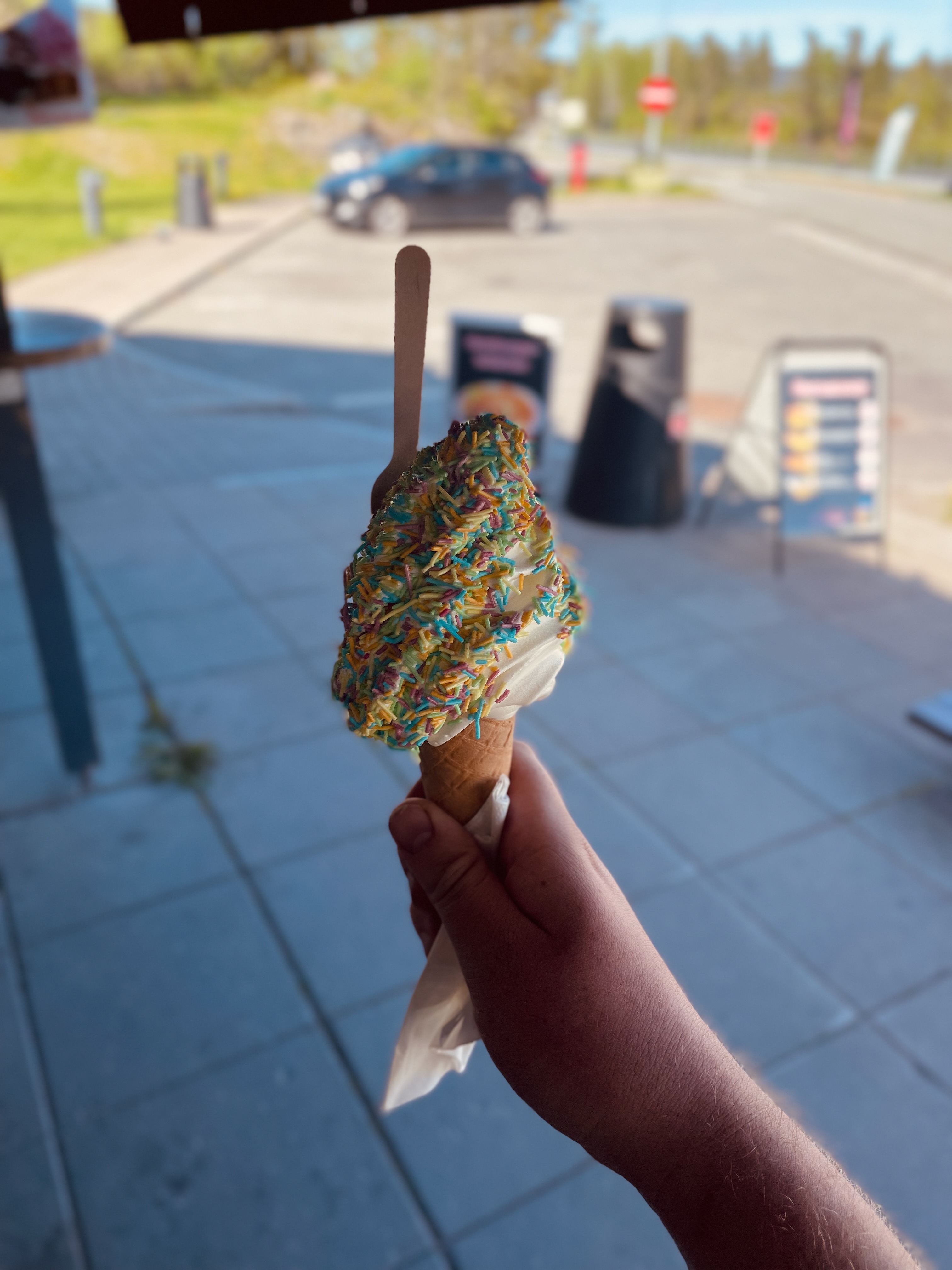 Tollerud rasteplass syd soft ice cream with colorful sprinkles held in front of the roadside parking area, showing the quick ice cream stop experience along the E18 in Norway