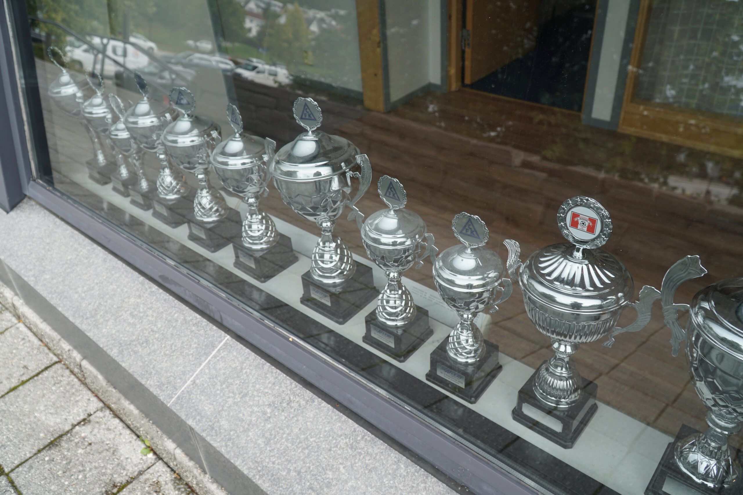 Aker Stadion Molde trophy display behind glass at the main entrance, showing multiple silver cups won by Molde FK arranged in a row inside the stadium building.