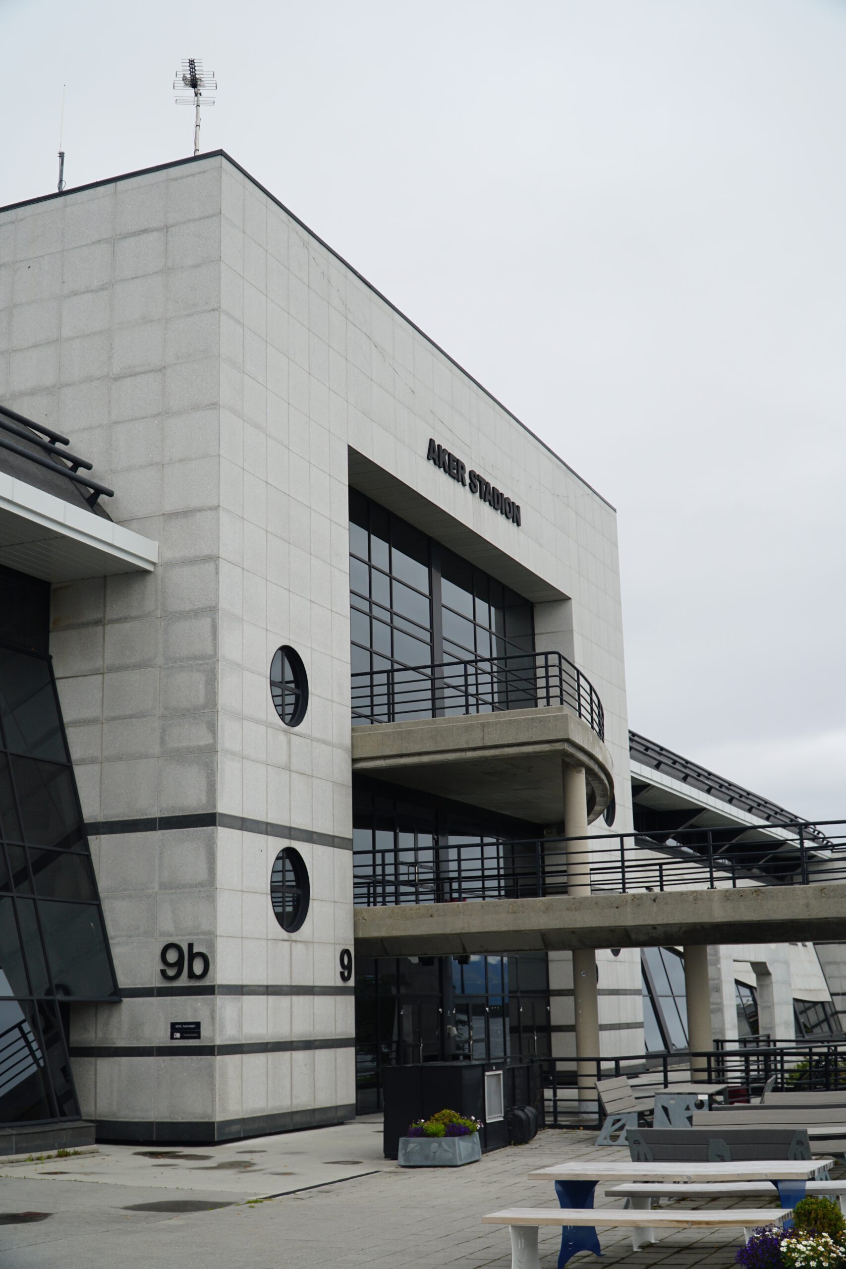 Aker Stadion Molde exterior facade with concrete architecture, balcony walkway, entrance numbers 9b and 9, and outdoor seating area in front of the Molde FK stadium.
