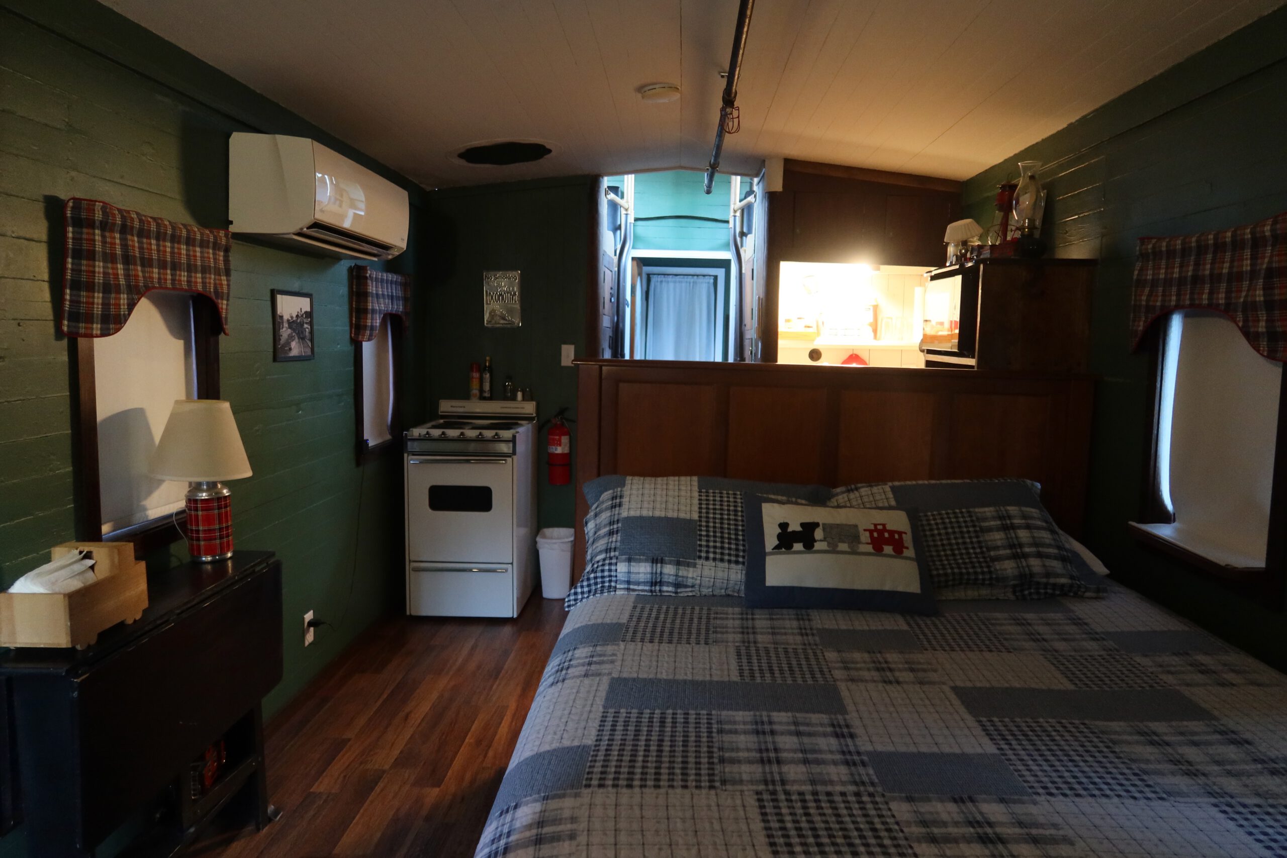Inside the Vacation Station caboose bedroom, cozy queen bed, compact kitchen and warm lighting, unique train Airbnb in Coulterville California