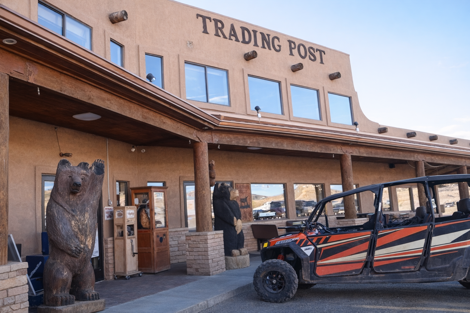 Old West–style Trading Post in Arizona with carved wooden bear statues at the entrance, rustic adobe facade, wooden beams, and an off-road side-by-side vehicle parked in front under a clear blue desert sky.