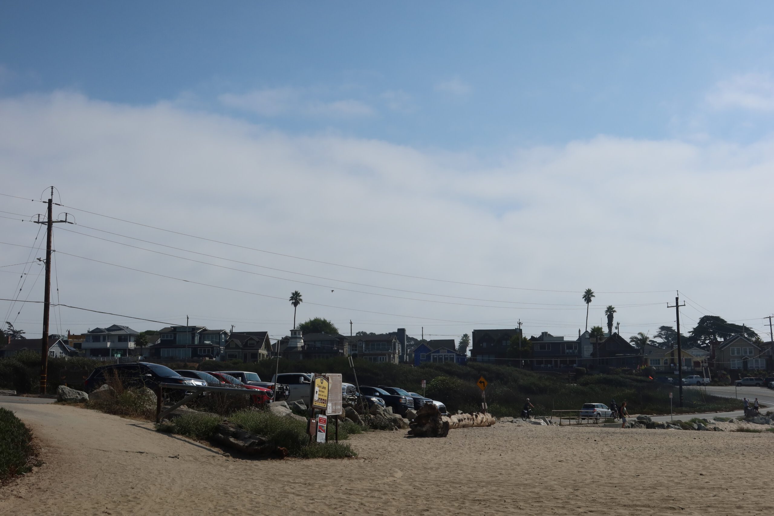 Parking area and beach access at Twin Lakes State Beach in Santa Cruz, California with coastal houses and palm trees in the background